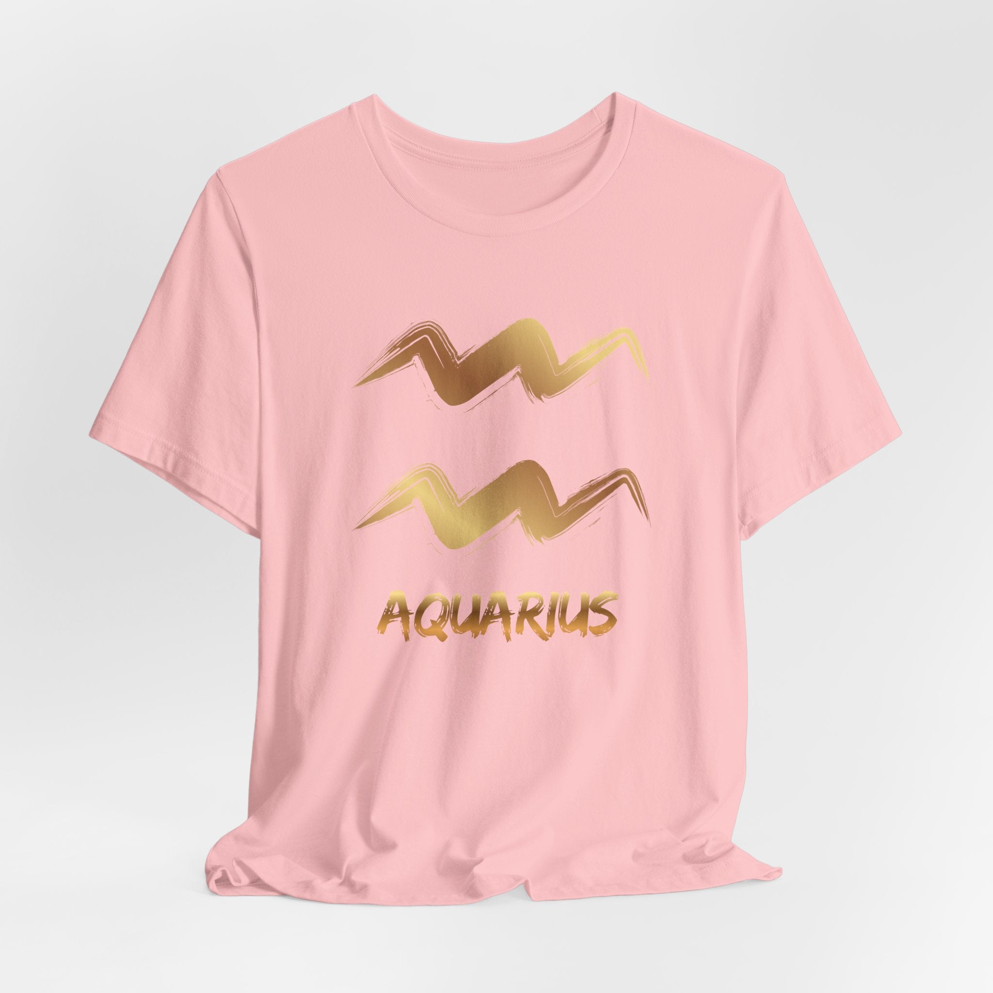 Pink t-shirt with gold Aquarius zodiac symbol on a light gray background