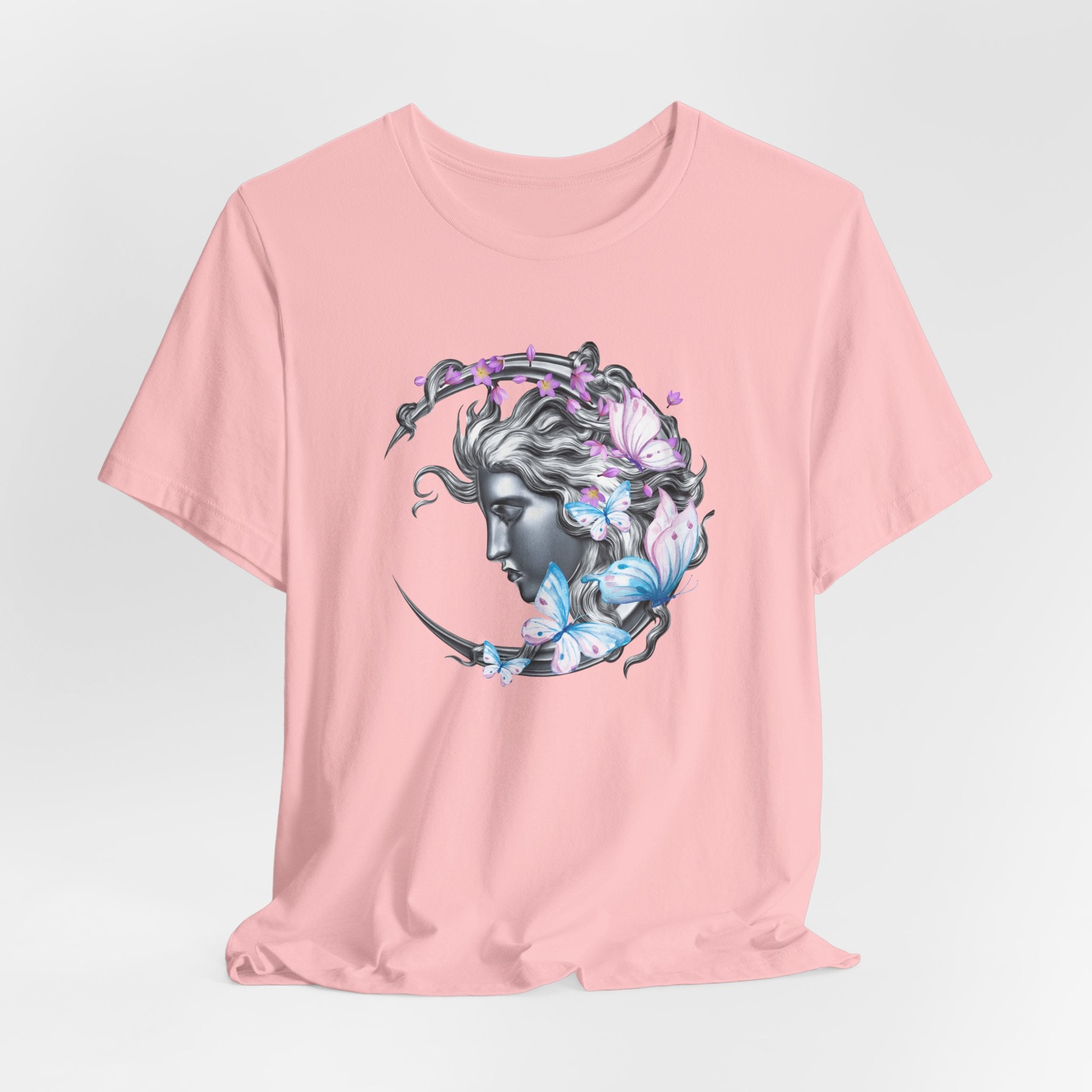 Pink t-shirt with a graphic design of a woman's head surrounded by butterflies on a light gray background.