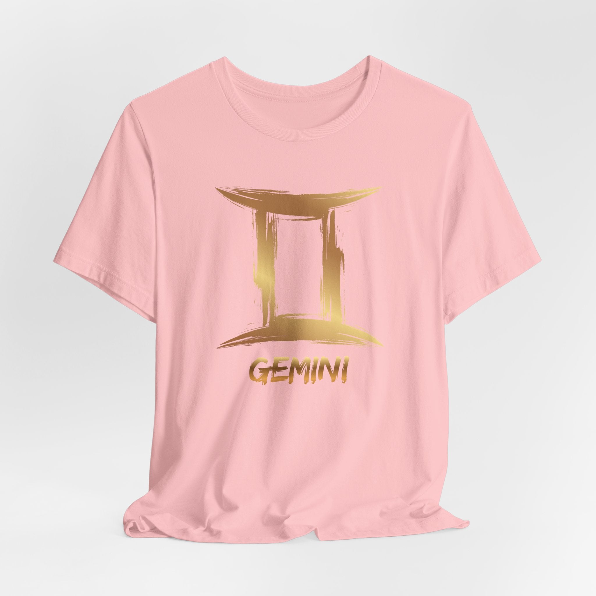 Pink t-shirt with gold Gemini zodiac sign design on a light gray background