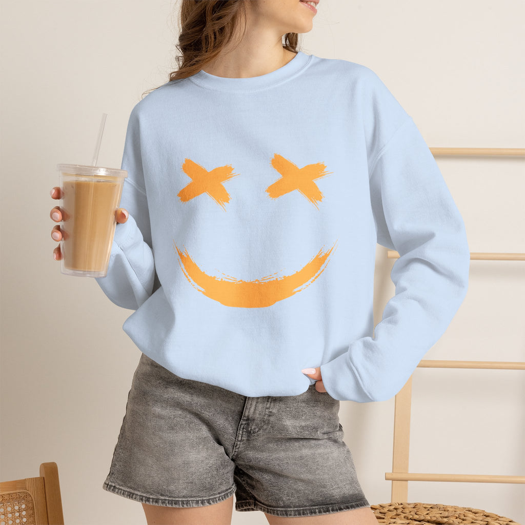 Person wearing a light blue sweatshirt with a smiley face design, holding a drink.