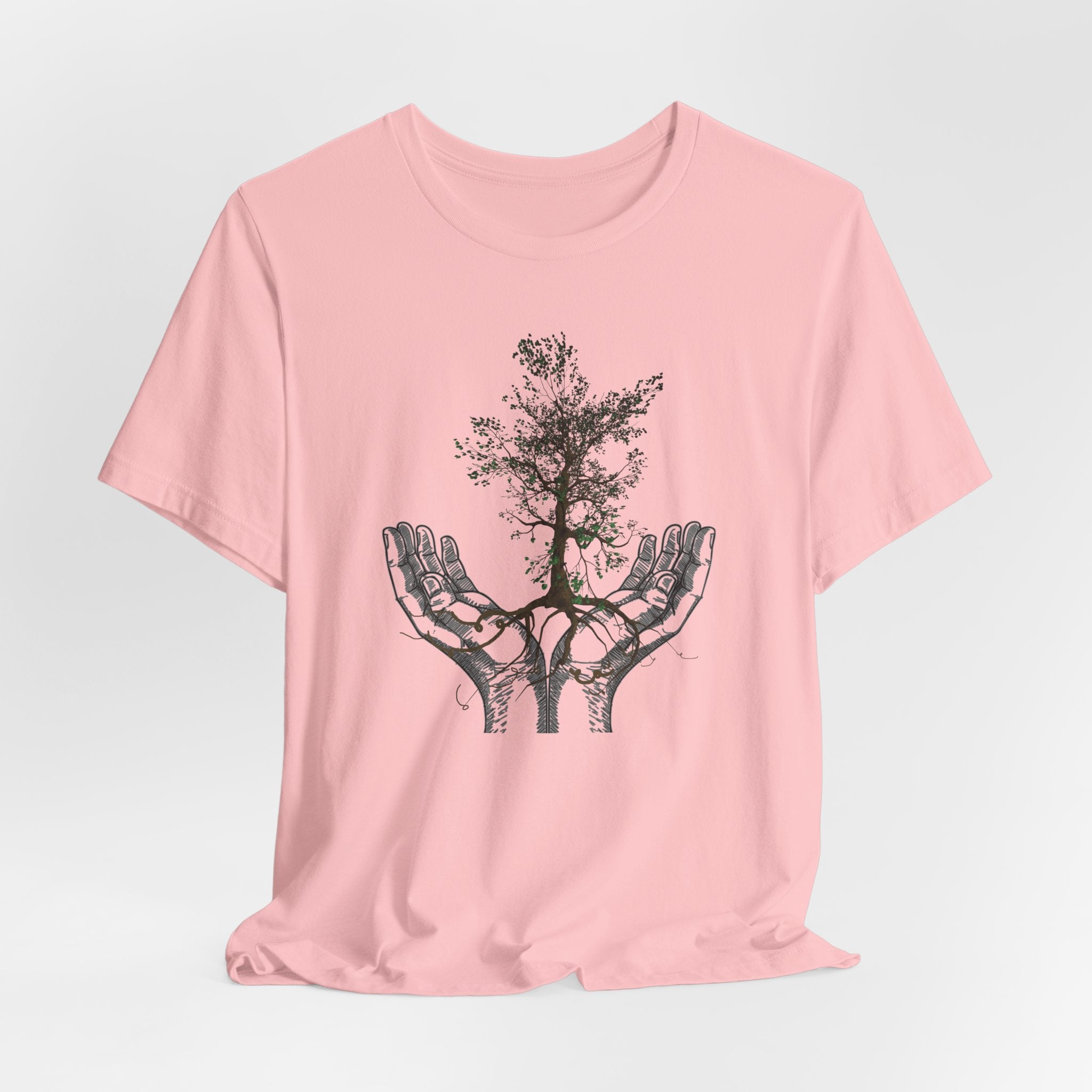 Pink t-shirt with a black tree design on hands against a light gray background