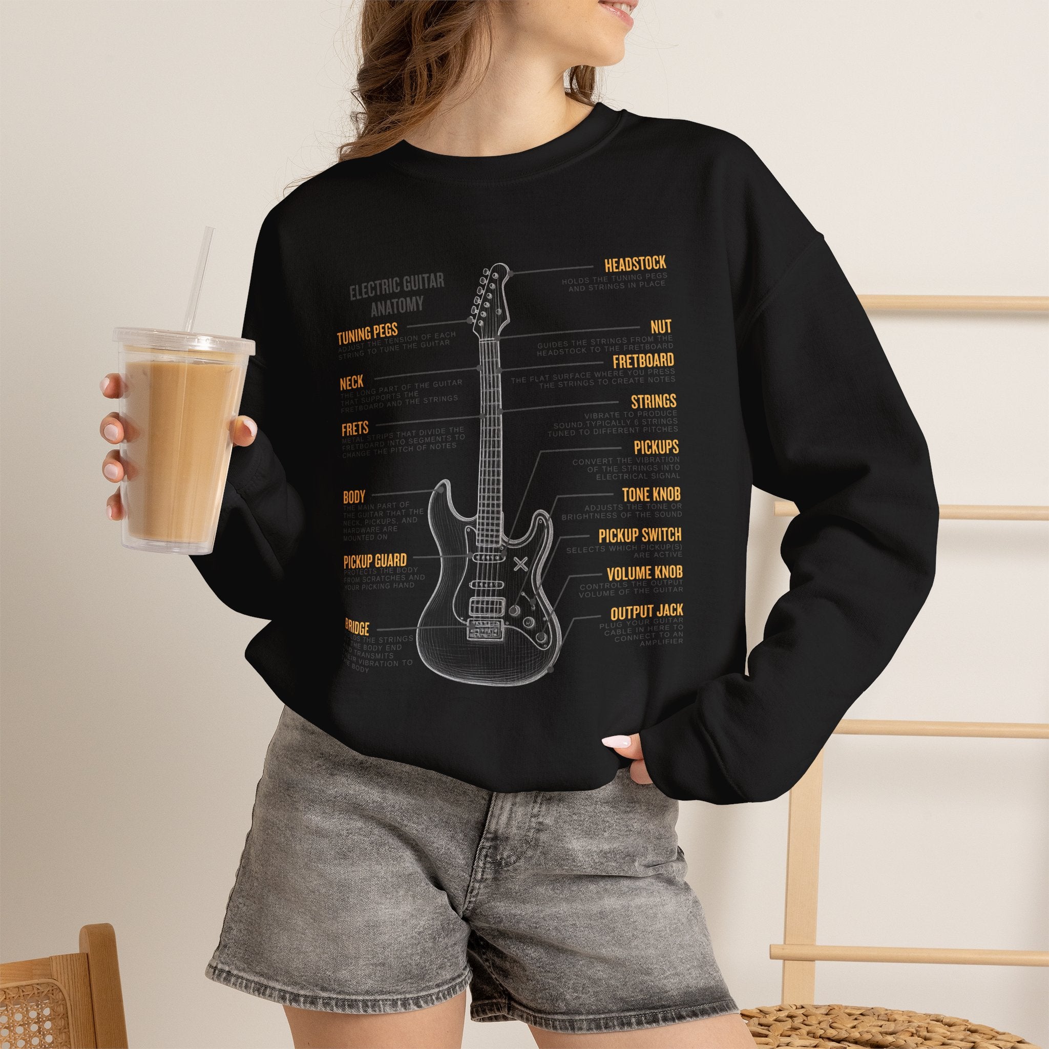 Person wearing a black sweatshirt with a electric guitar anatomy diagram design, holding a drink.