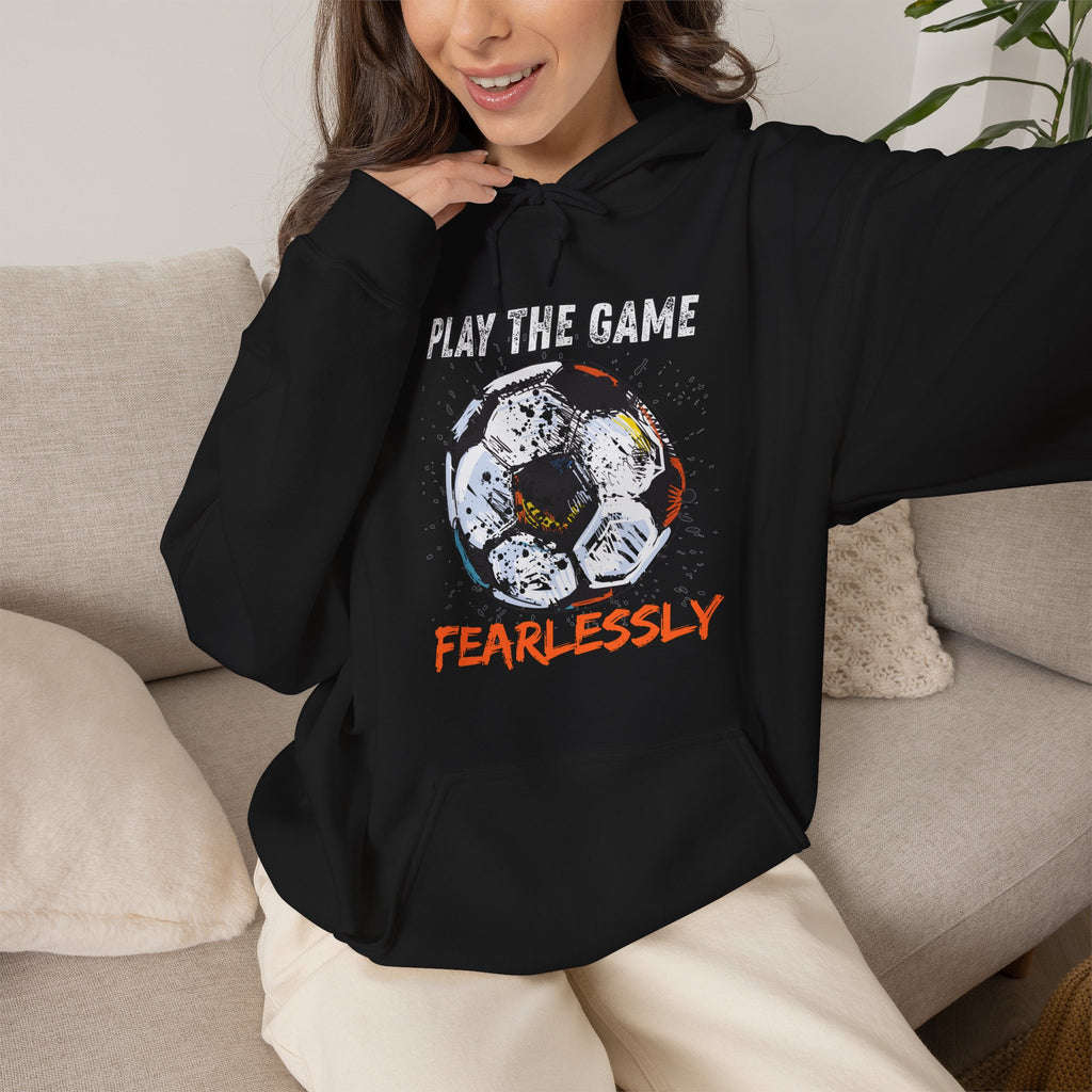 A woman wearing black hoodie with dirty soccer ball graphic and play the game fearlessly text on a white background