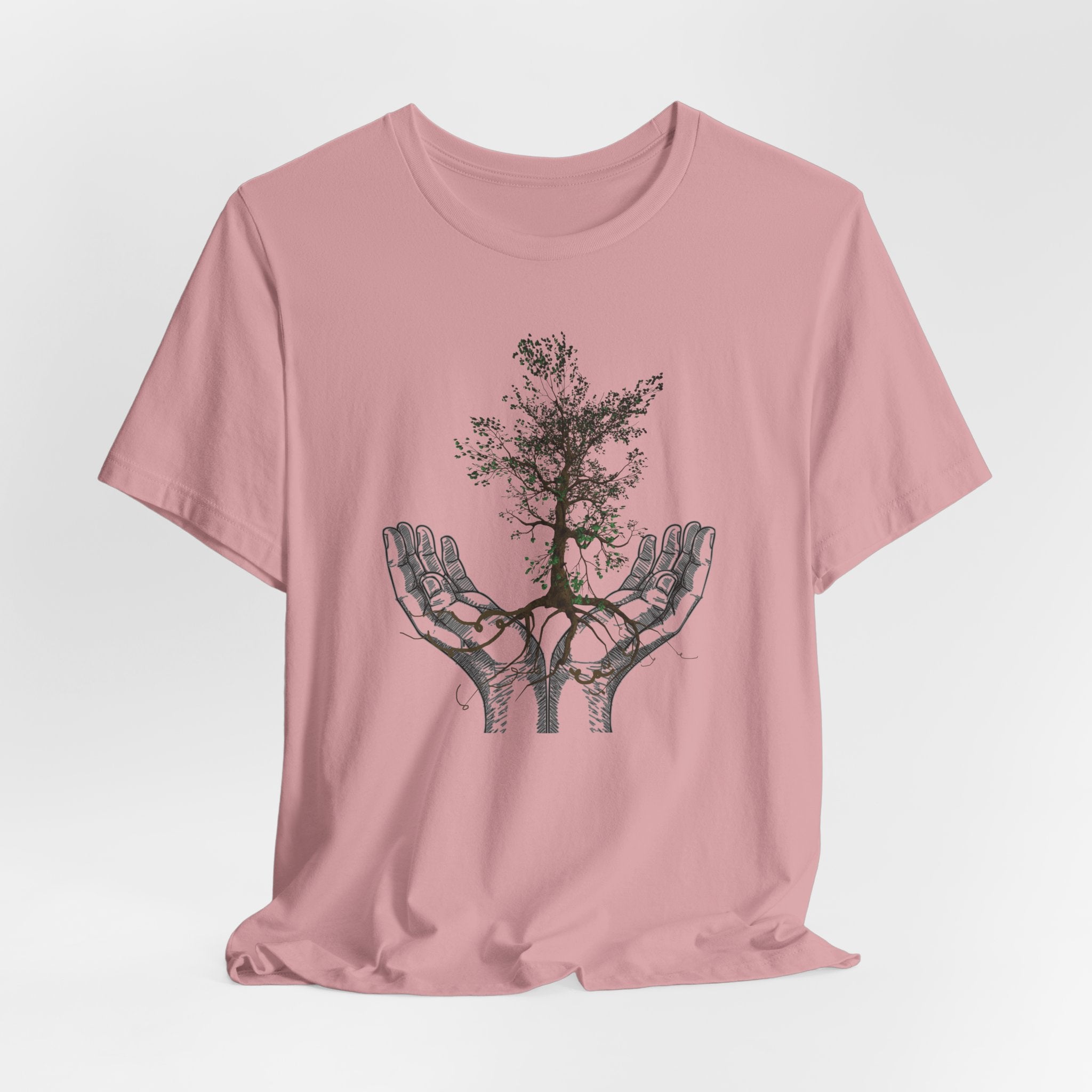 Pink t-shirt with a tree design in hands on a light gray background