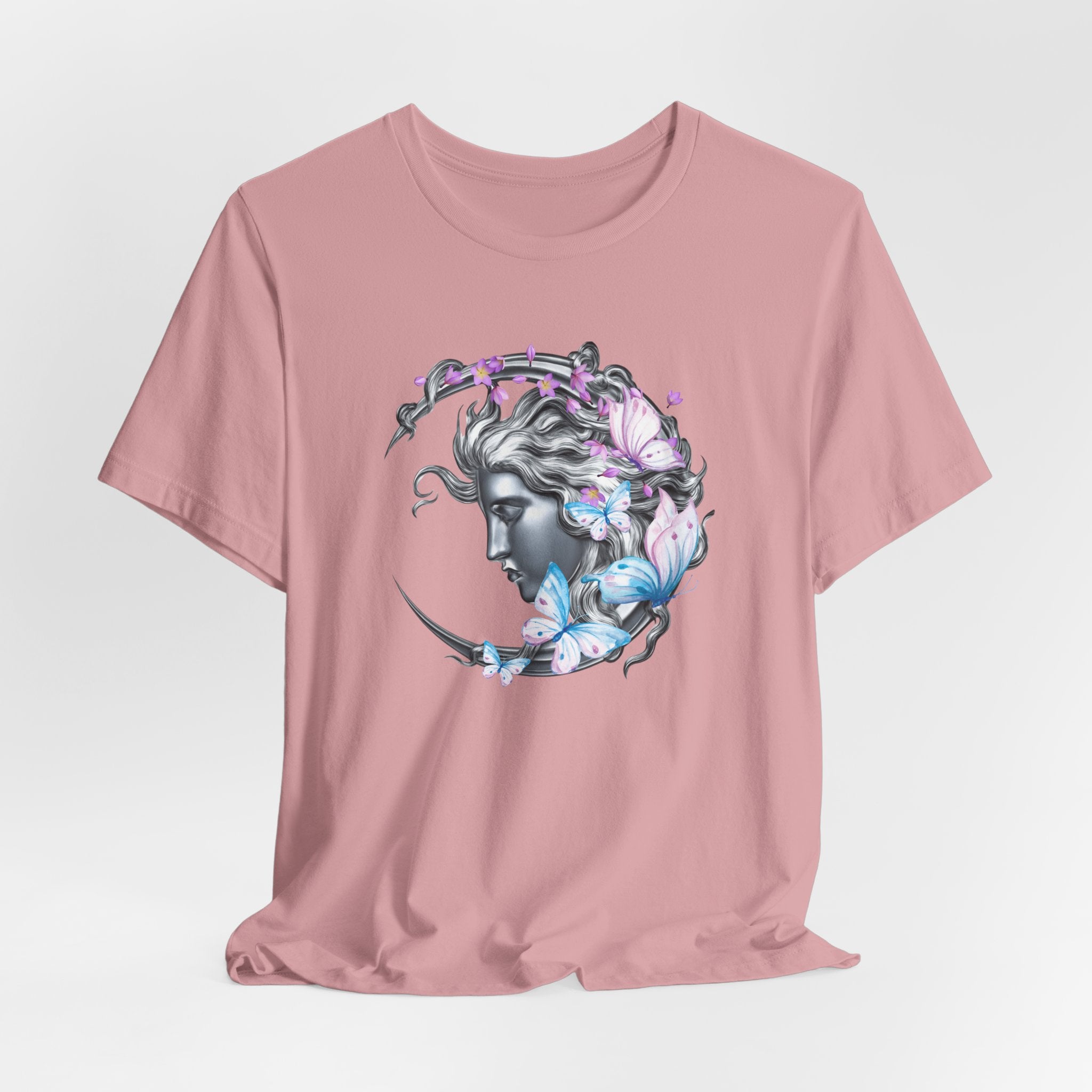 Pink t-shirt with a graphic design of a woman's face surrounded by butterflies on a light gray background.