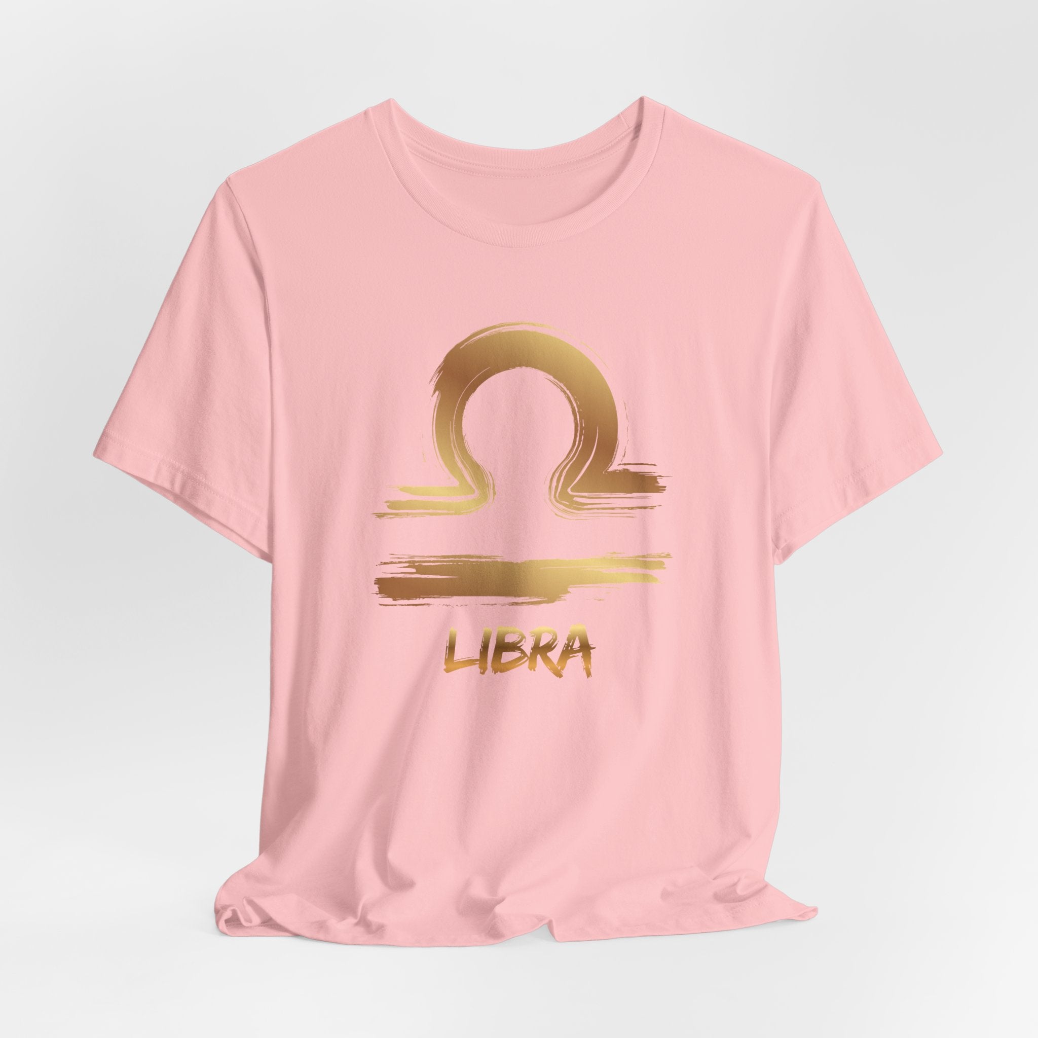 Pink t-shirt with gold Libra zodiac symbol on a light gray background