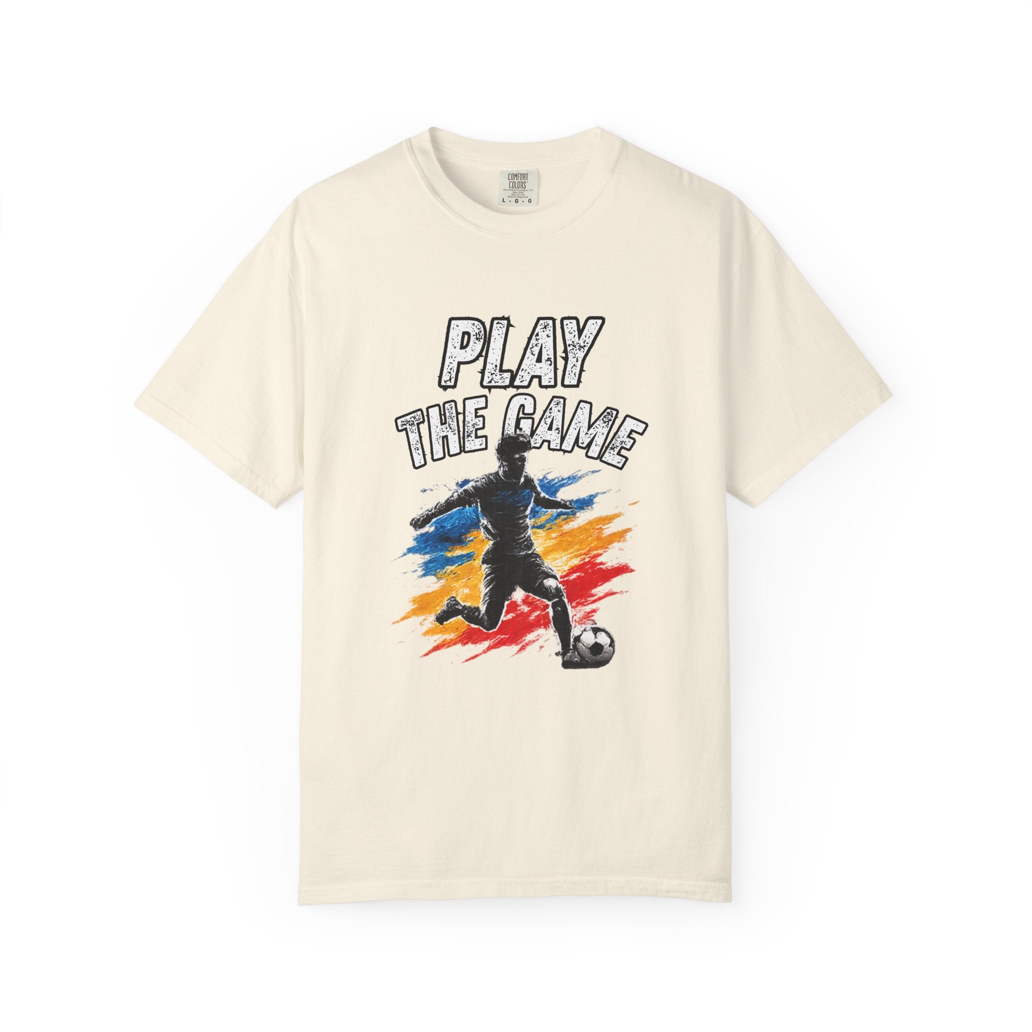 An off-white short-sleeve t-shirt with a graphic print on the front. The graphic features the text 'PLAY THE GAME' above a stylized soccer player silhouette running past a soccer ball, set against a background of blue, orange, and red paint strokes.