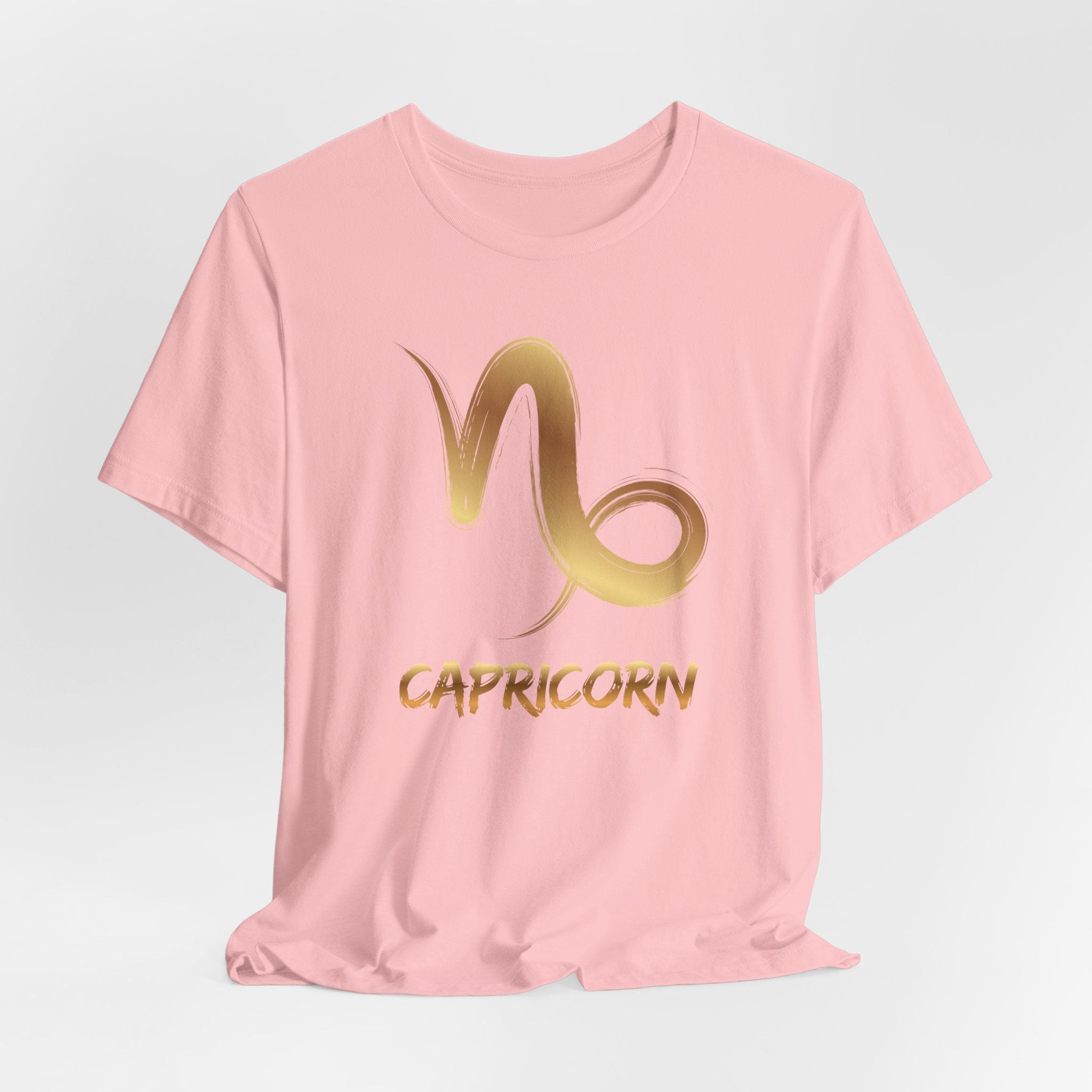Pink t-shirt with gold Capricorn symbol on a light gray background