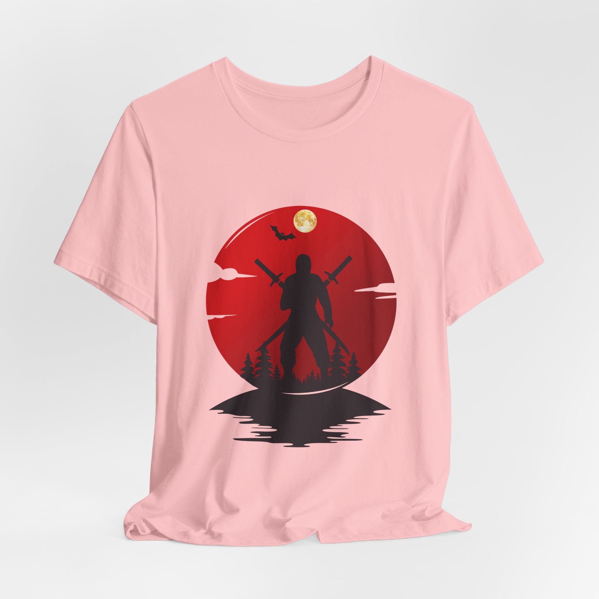 Pink t-shirt with a red circular design featuring a silhouette of a person holding two swords against a moonlit sky.