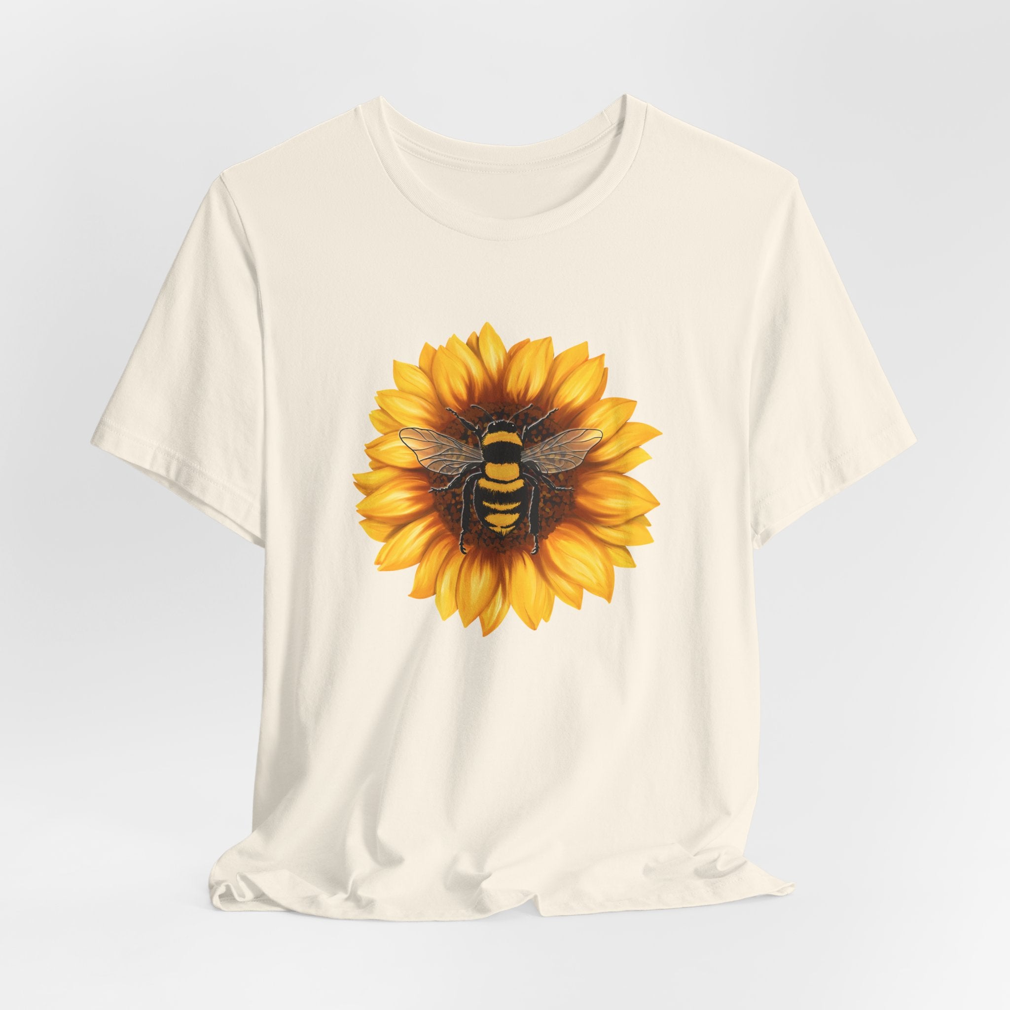 White t-shirt with a sunflower and bee design on a light gray background