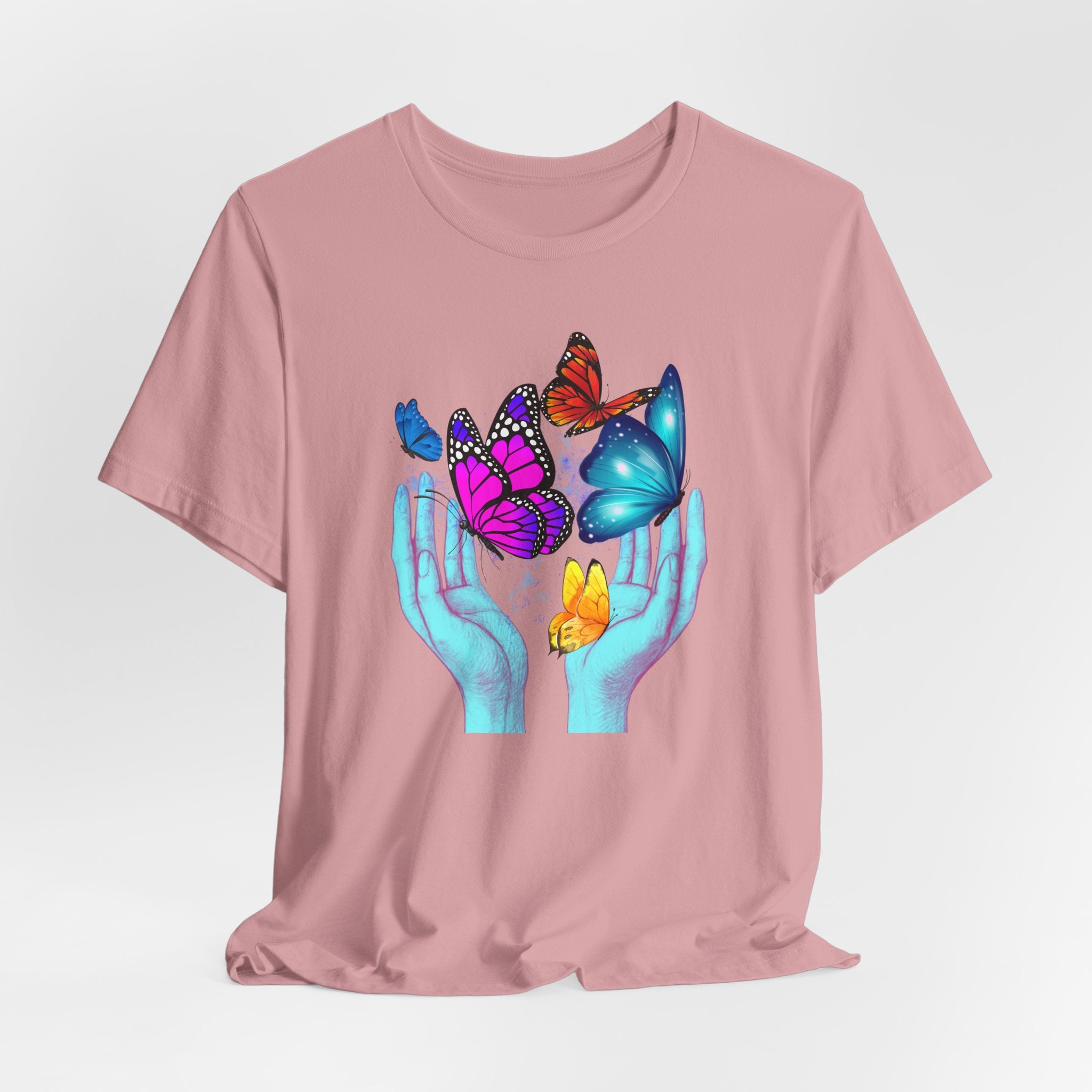 Pink t-shirt with a graphic of hands holding butterflies on a light gray background