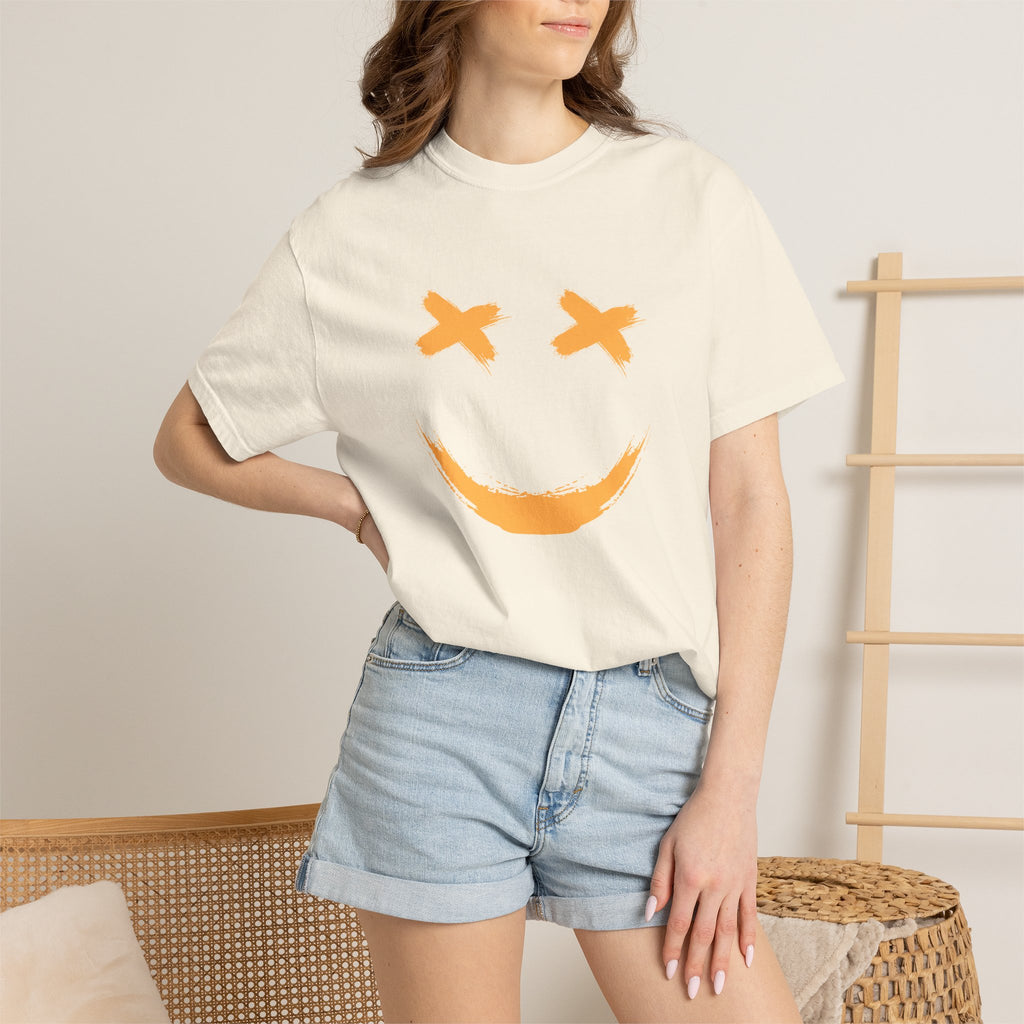Person wearing a cream t-shirt with a smiley face design and denim shorts in a casual setting.