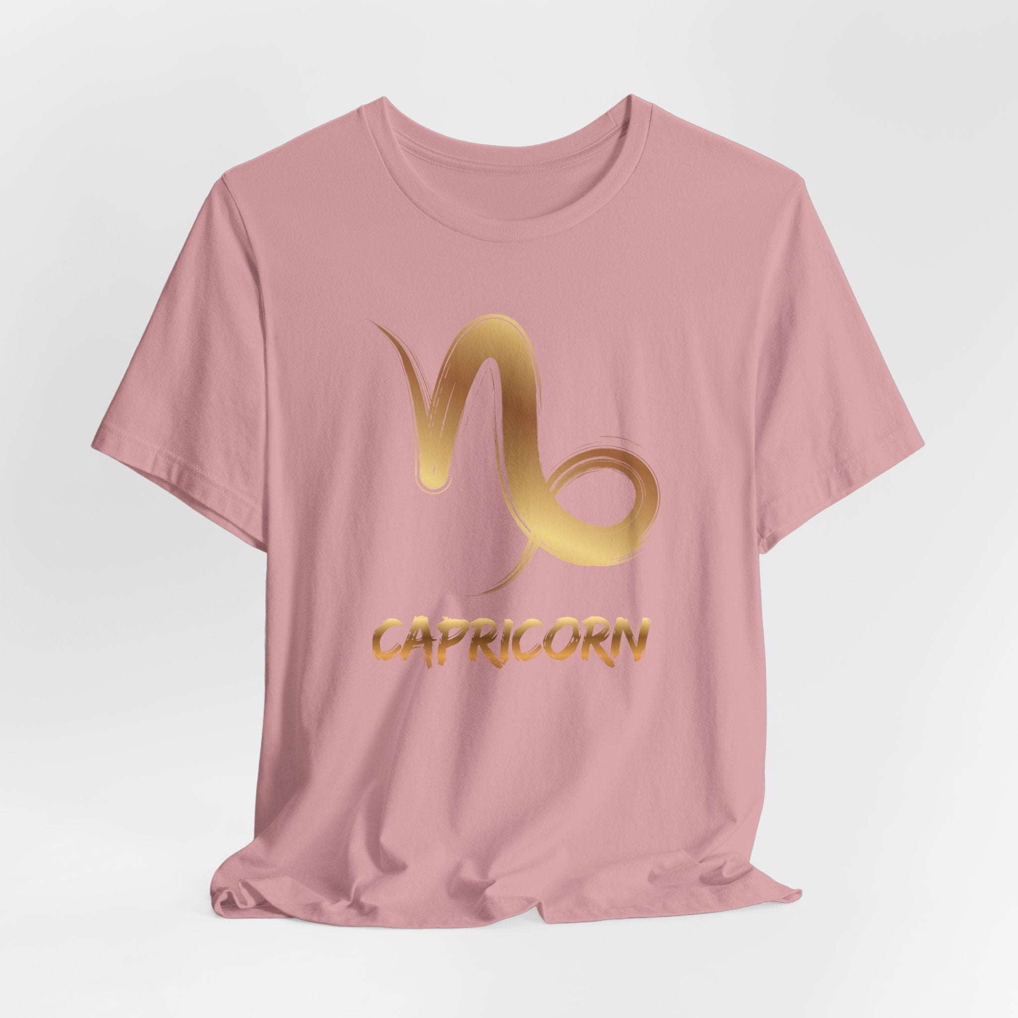 Pink t-shirt with gold Capricorn symbol on a light gray background