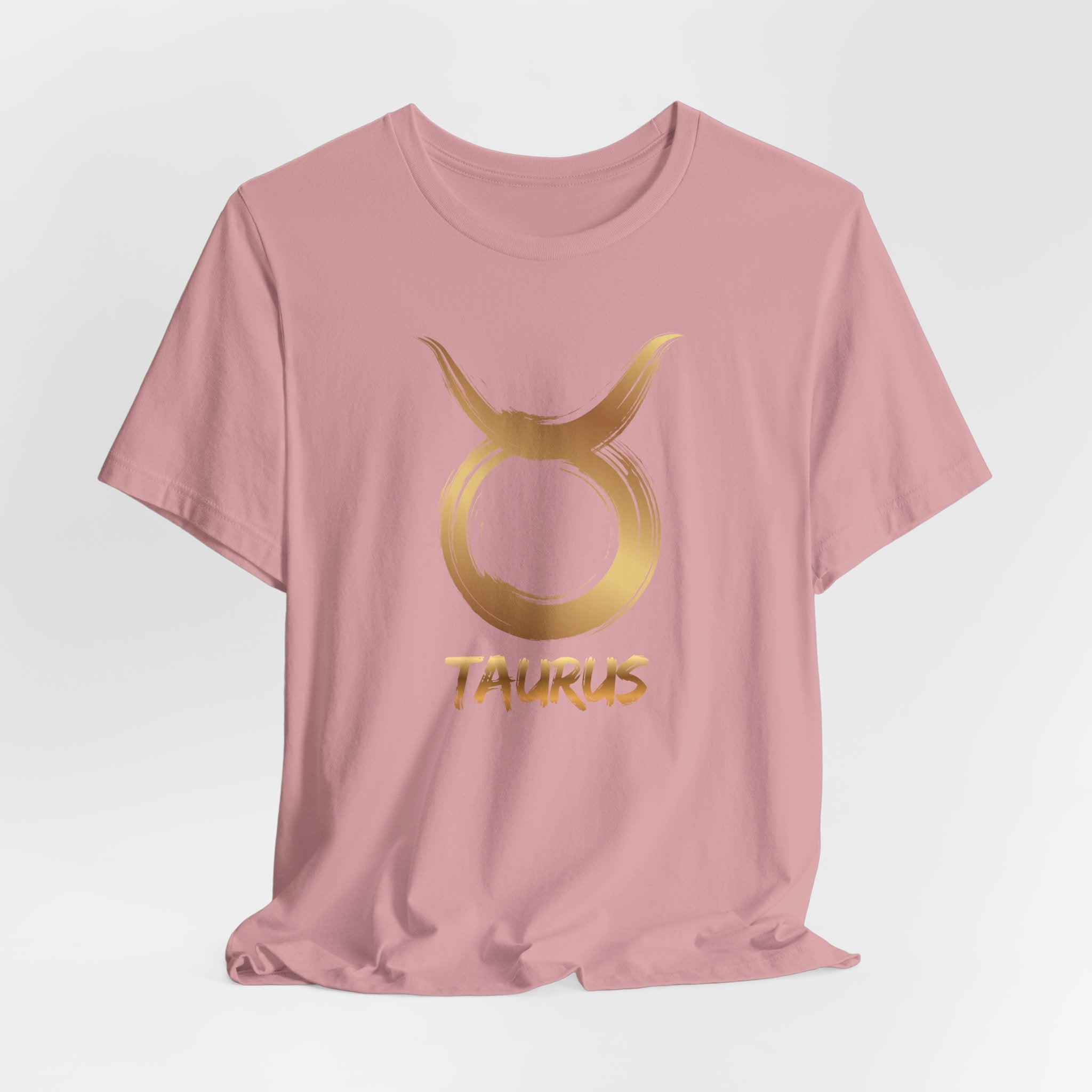 Pink t-shirt with gold Taurus symbol and text on a light gray background