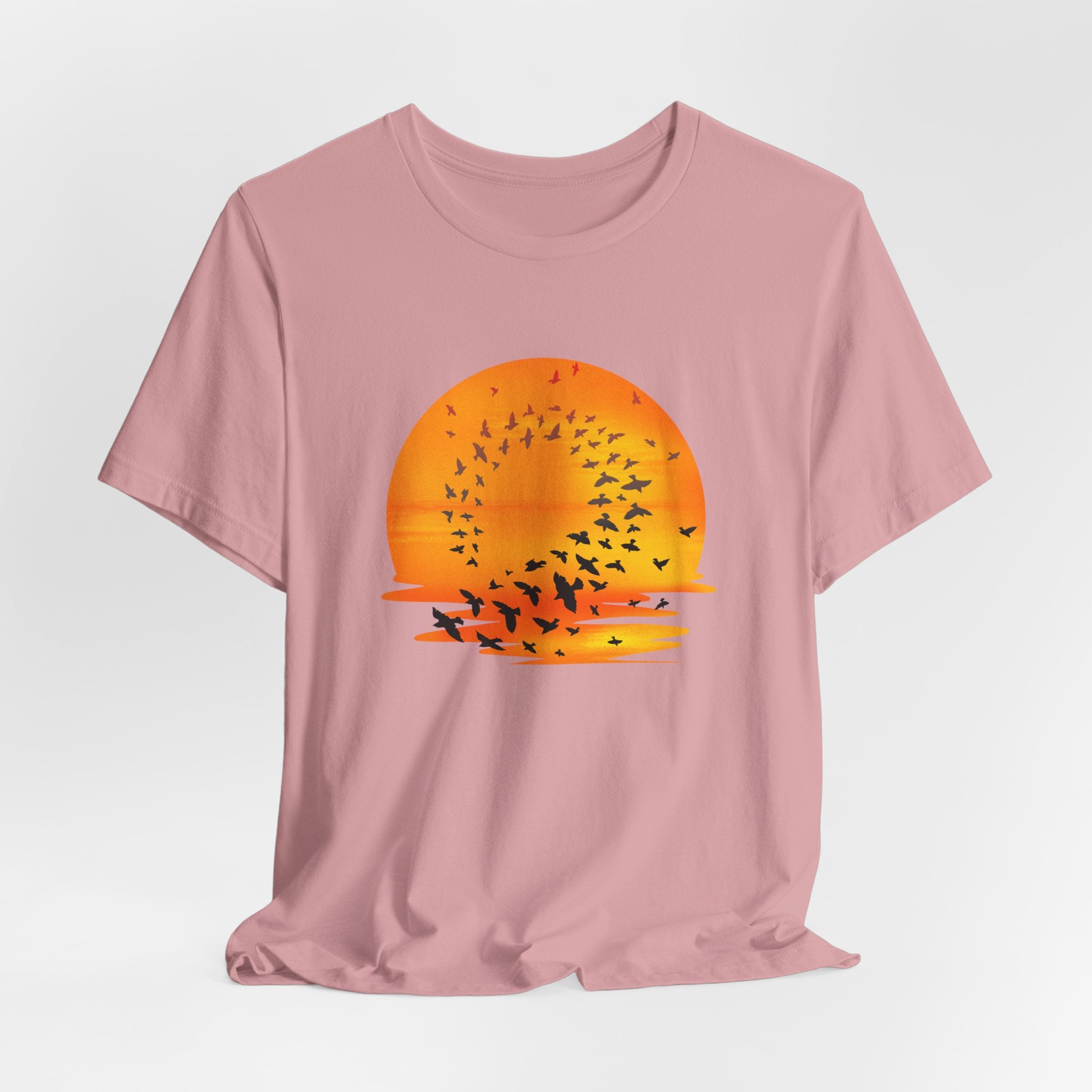 Pink t-shirt with a sunset and bird design on a light gray background