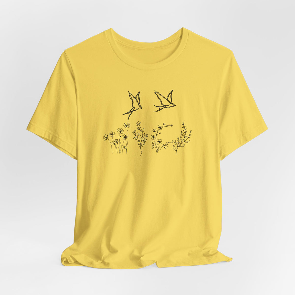 Yellow t-shirt with black floral and bird design on a light gray background