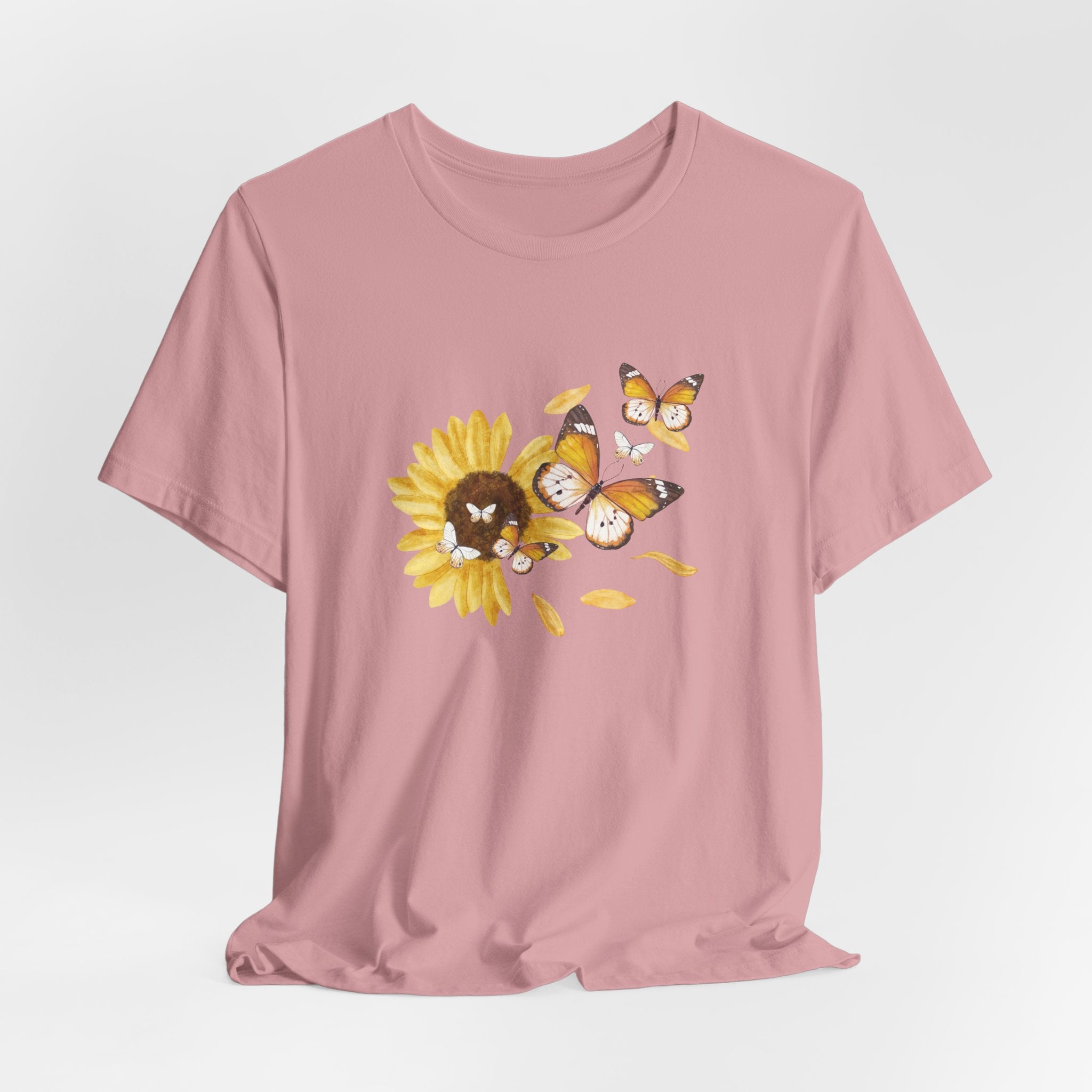 Pink t-shirt with a sunflower and butterfly graphic on a light gray background