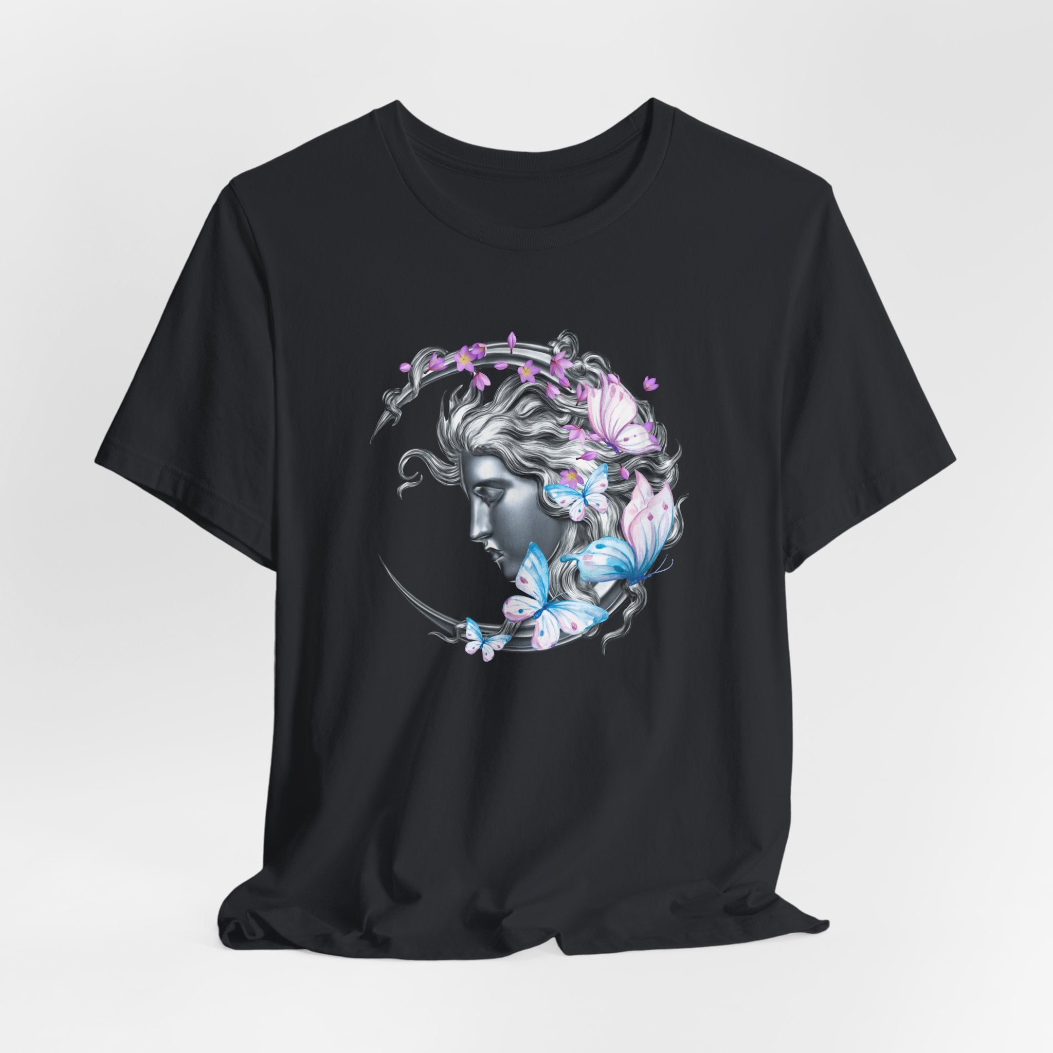 Black t-shirt with a decorative design of a woman's face on a crescent moon with butterflies and flowers, on a light gray background.