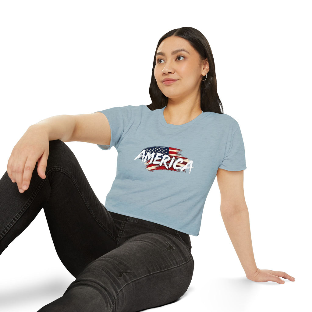 Woman wearing a light blue t-shirt with 'AMERICA' and an American flag design, sitting on a white background.