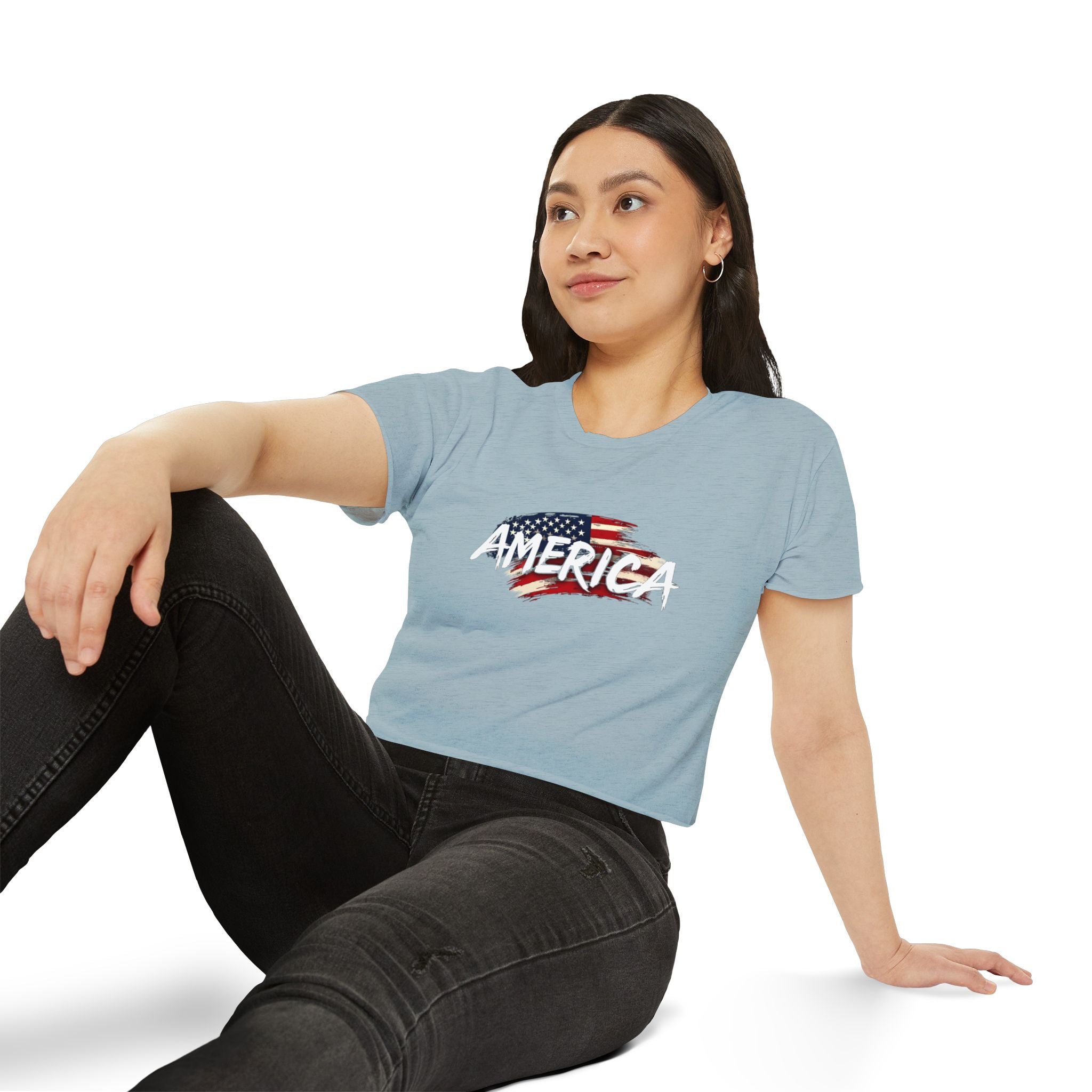 Woman wearing a light blue t-shirt with 'AMERICA' and an American flag design, sitting on a white background.