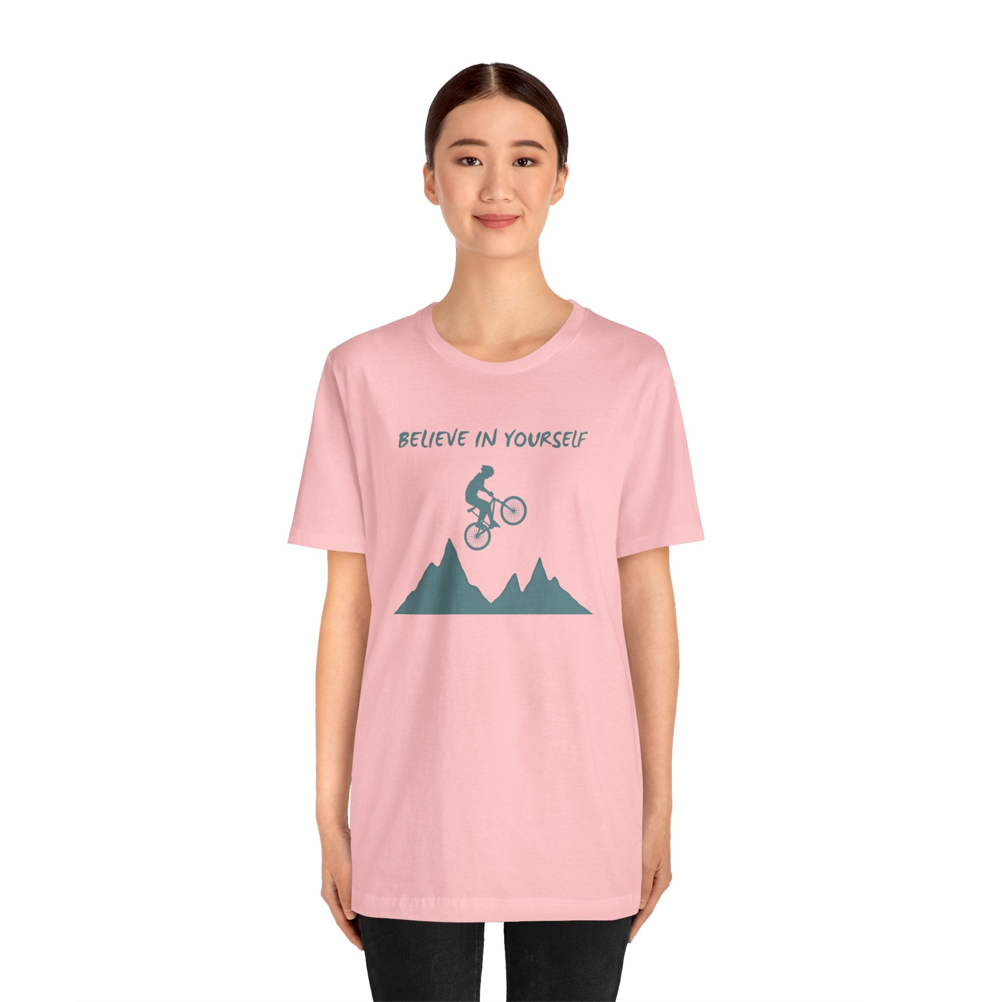 Person wearing a pink t-shirt with a mountain and bicycle graphic and text on a white background