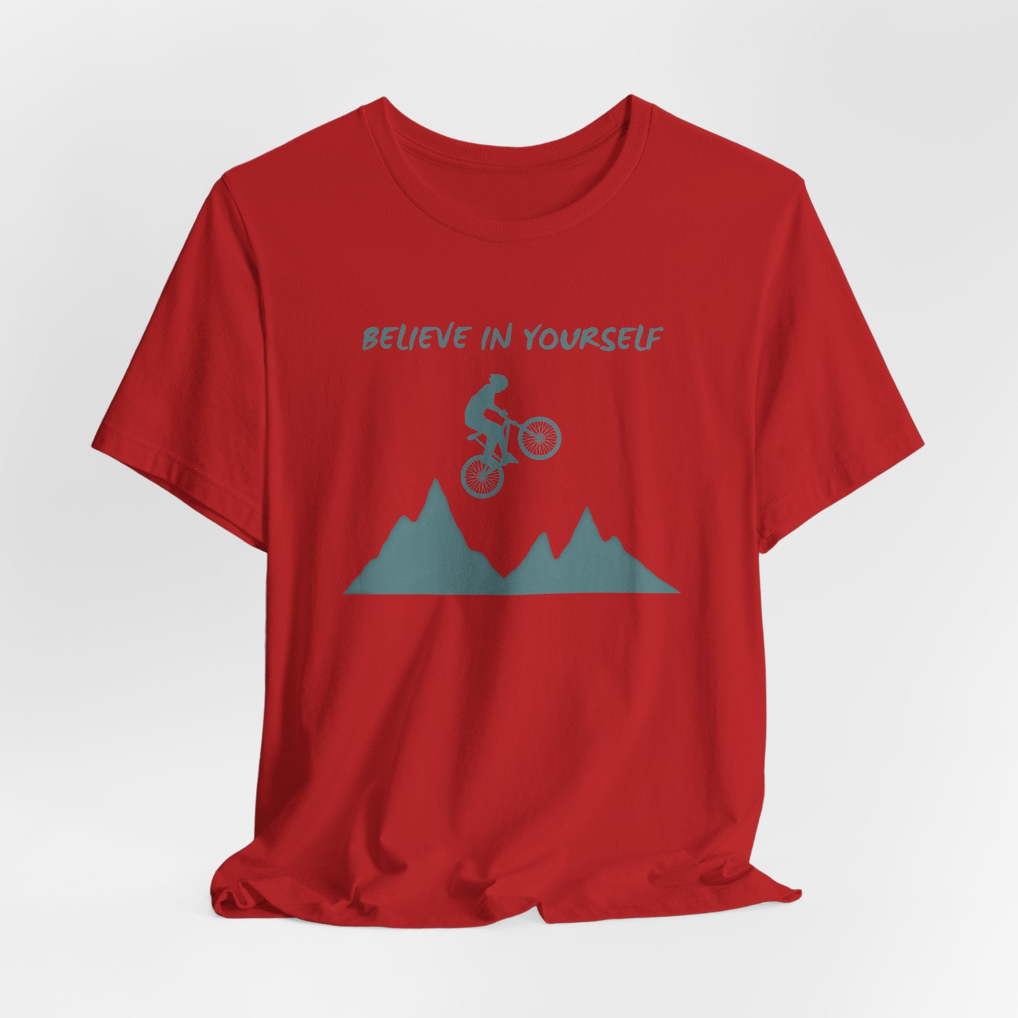Red t-shirt with mountain and bike graphic and 'Believe in Yourself' text on a white background