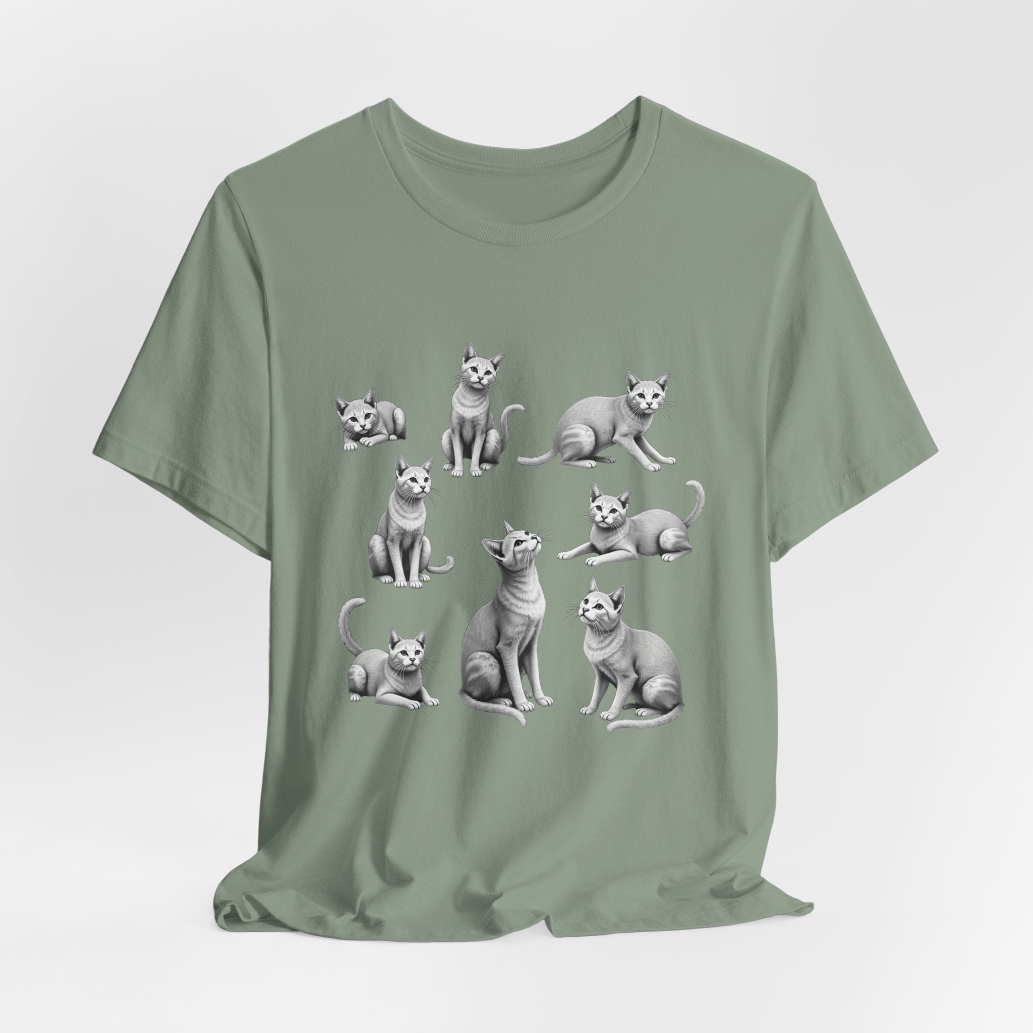 Sage green t-shirt with cat illustrations on a light gray background
