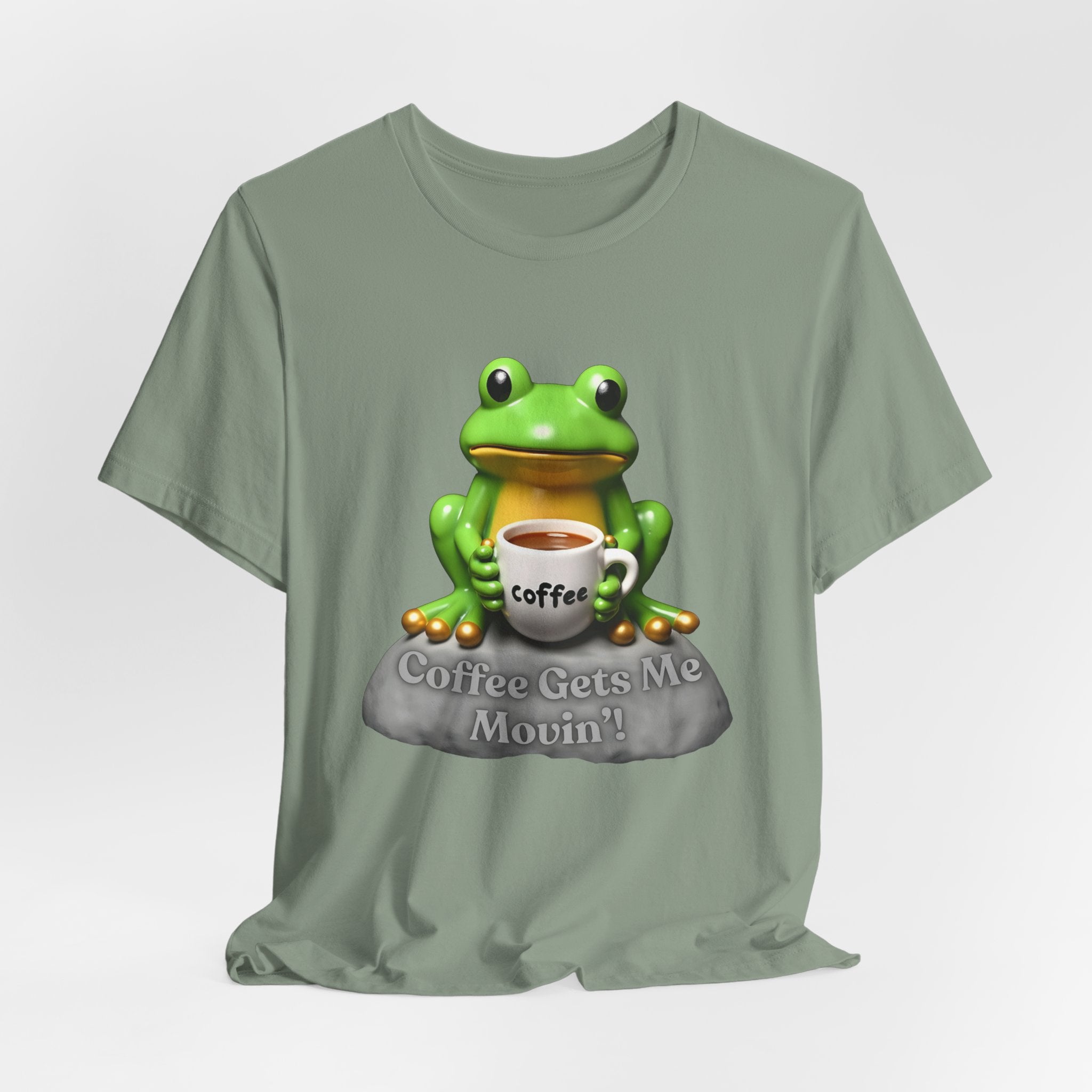 Sage green t-shirt with a green frog holding a coffee cup and 'Coffee Gets Me Movin'' text on a white background