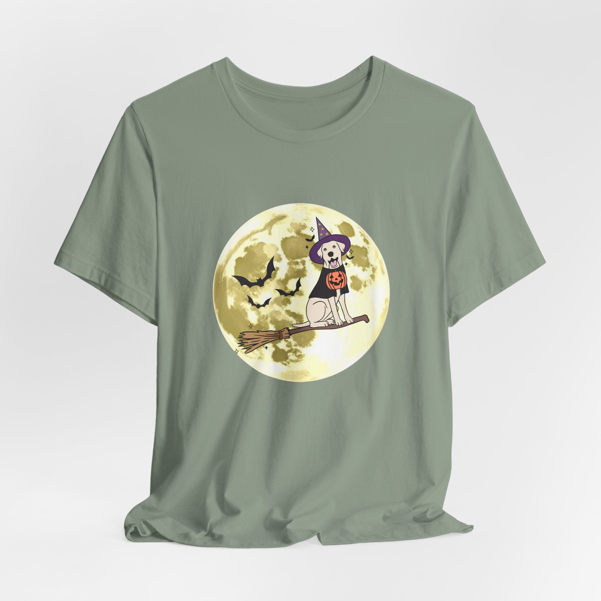 Sage green t-shirt with Halloween design featuring bats and a dog in a witch hat and pumpkin on a broomstick against a moonlit sky.
