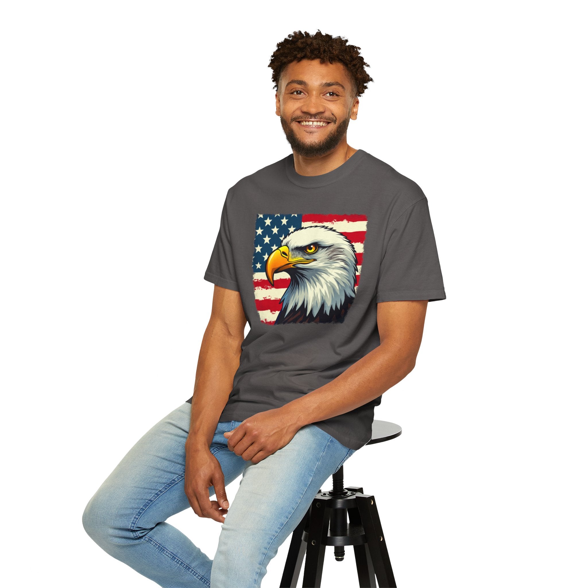 Man wearing a gray t-shirt with an eagle and American flag design, sitting on a stool against a white background.