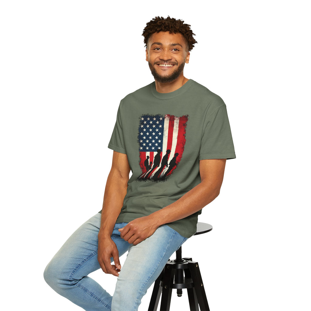 Man wearing a green t-shirt with an American flag design, sitting on a stool against a white background