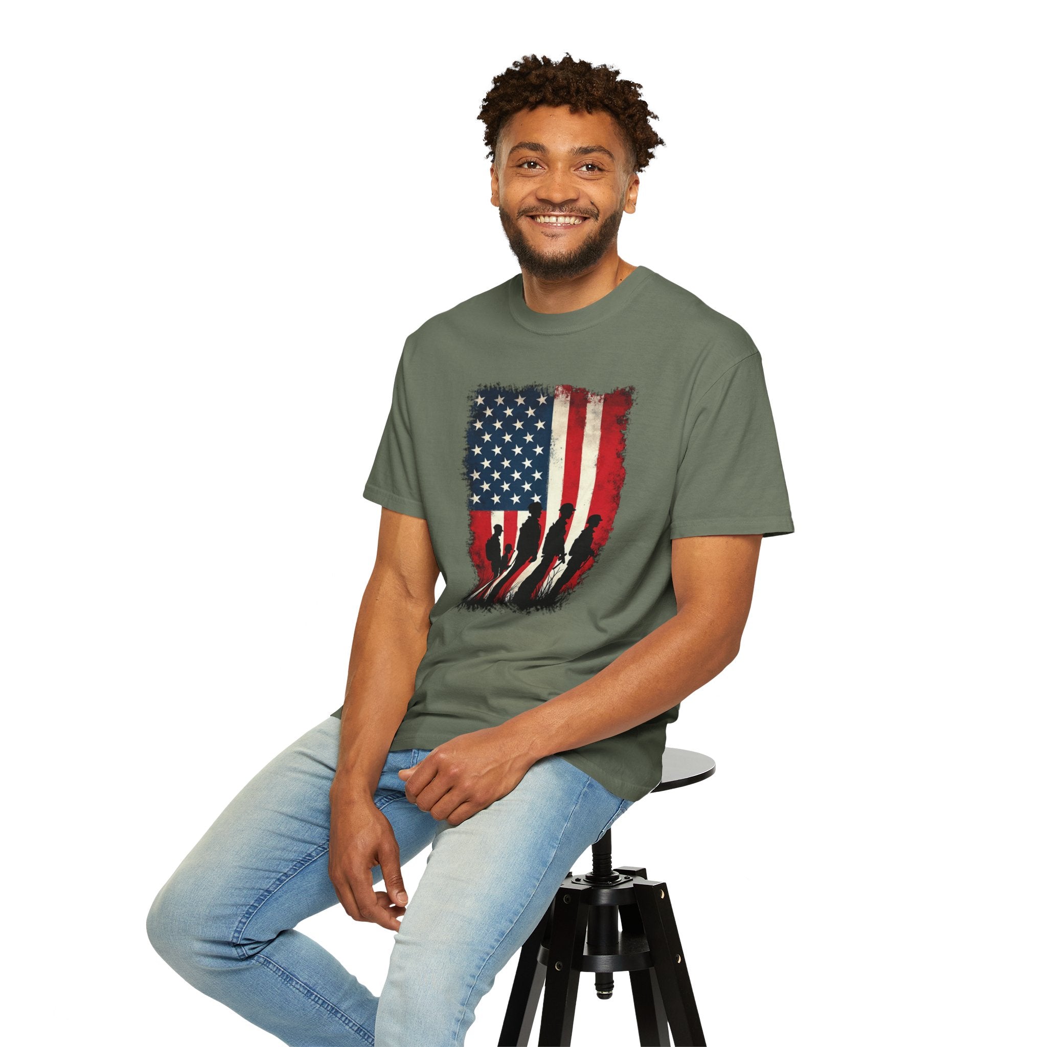 Man wearing a green t-shirt with an American flag design, sitting on a stool against a white background