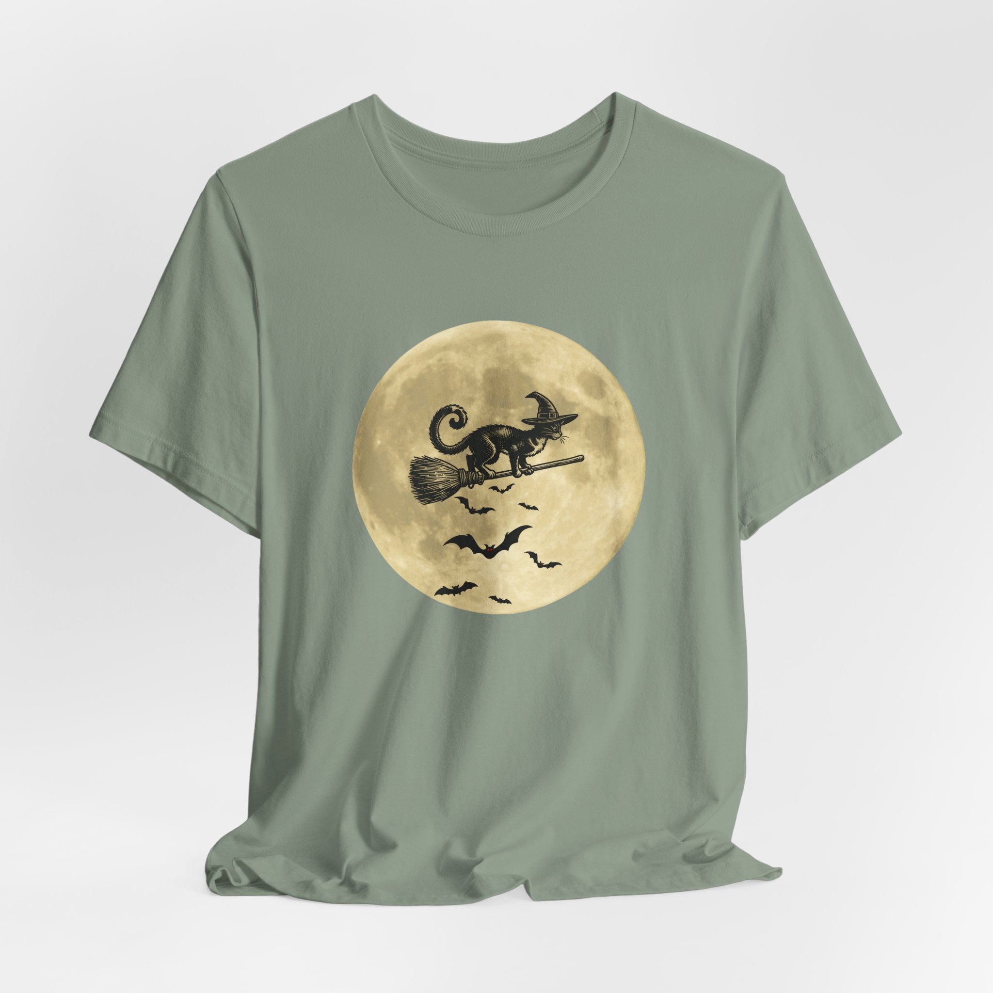 Sage green t-shirt with a Halloween design of a cat on a broomstick against a moon background.