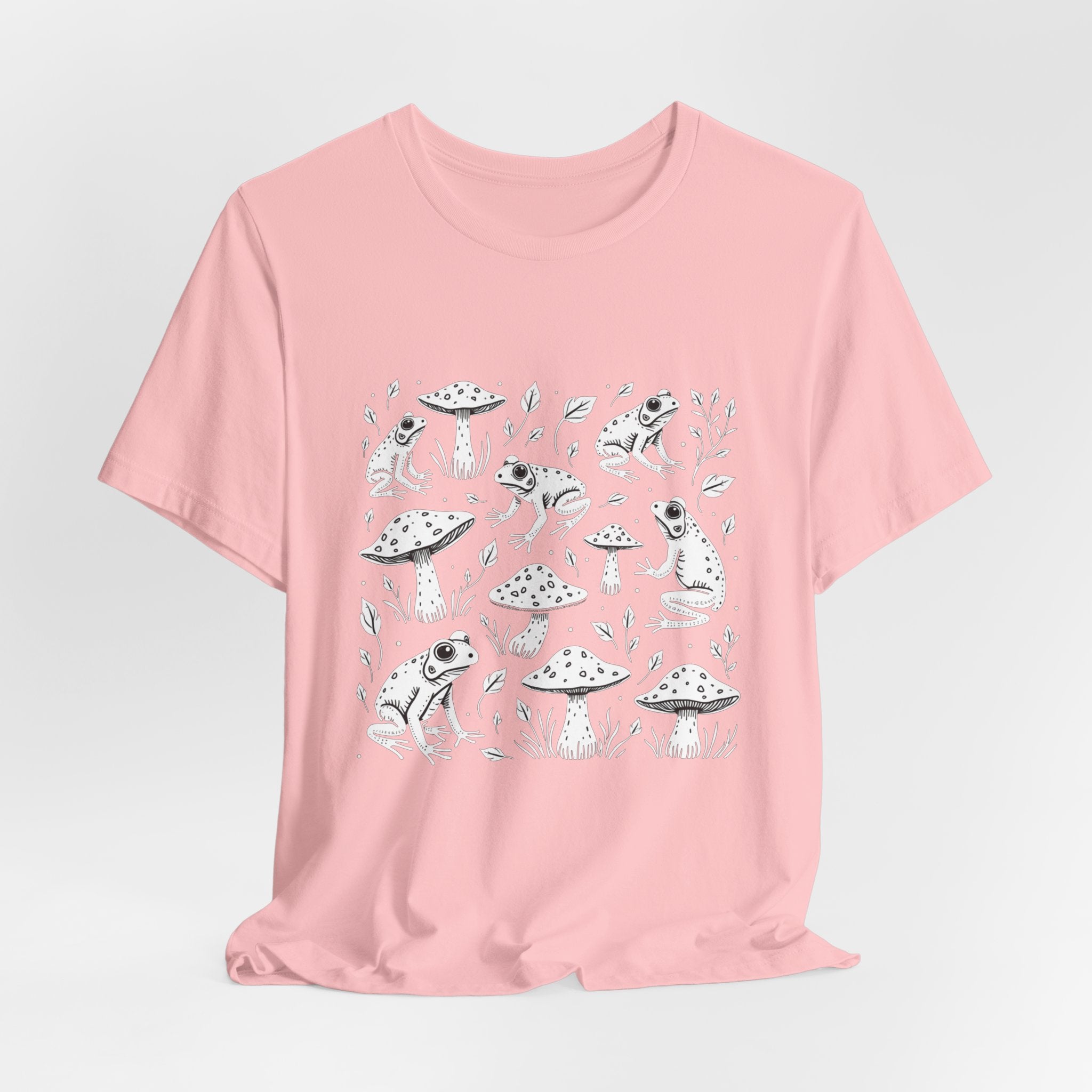 Pink t-shirt with white frogs, grass and mushroom design on a white background