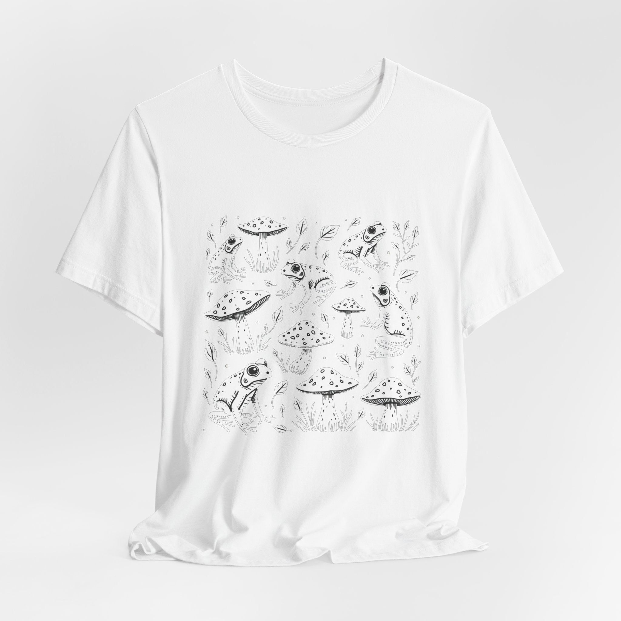 White t-shirt with white frogs, grass and mushroom design on a white background