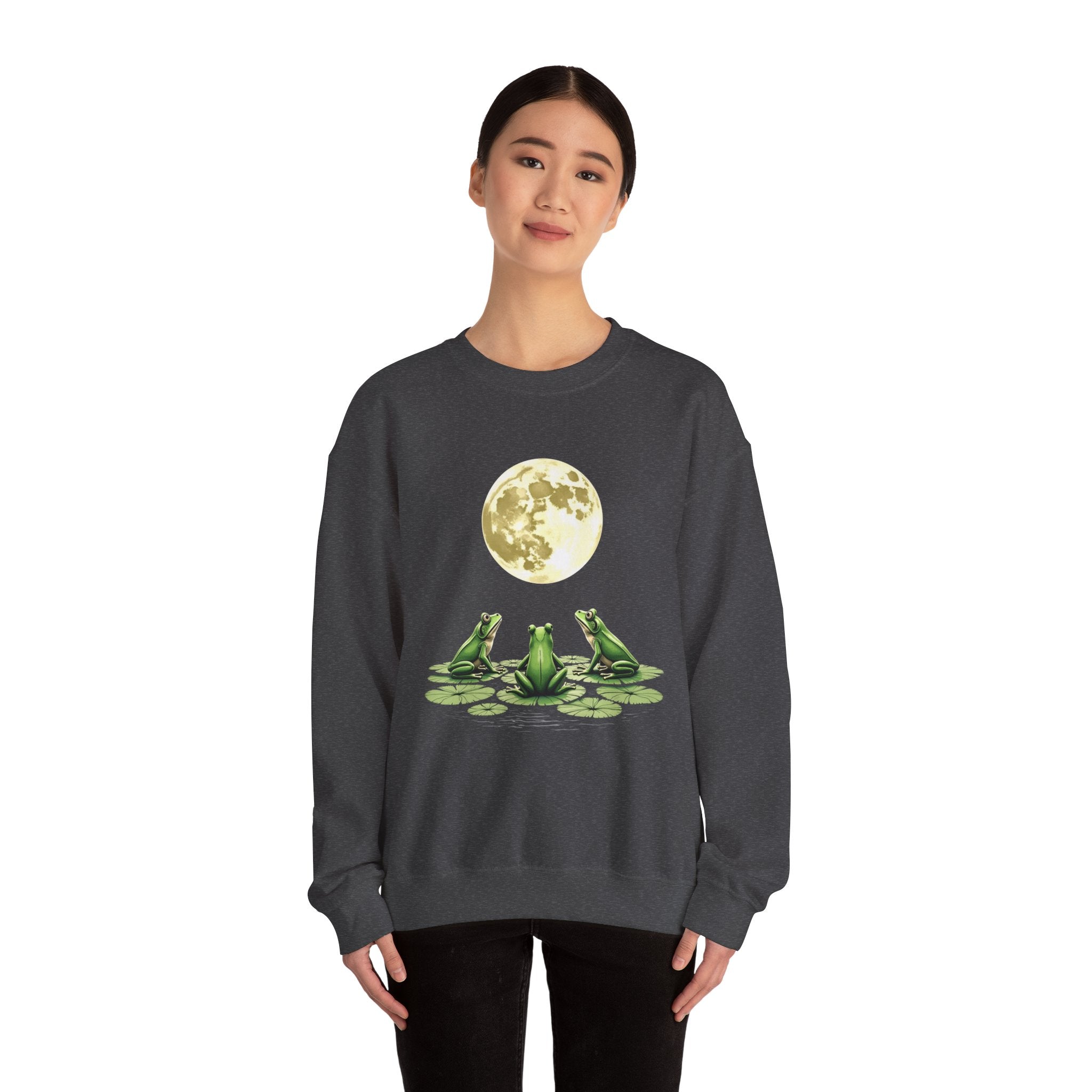 Person wearing a dark gray sweatshirt with a graphic of three frogs on lily pads and a moon in the background.