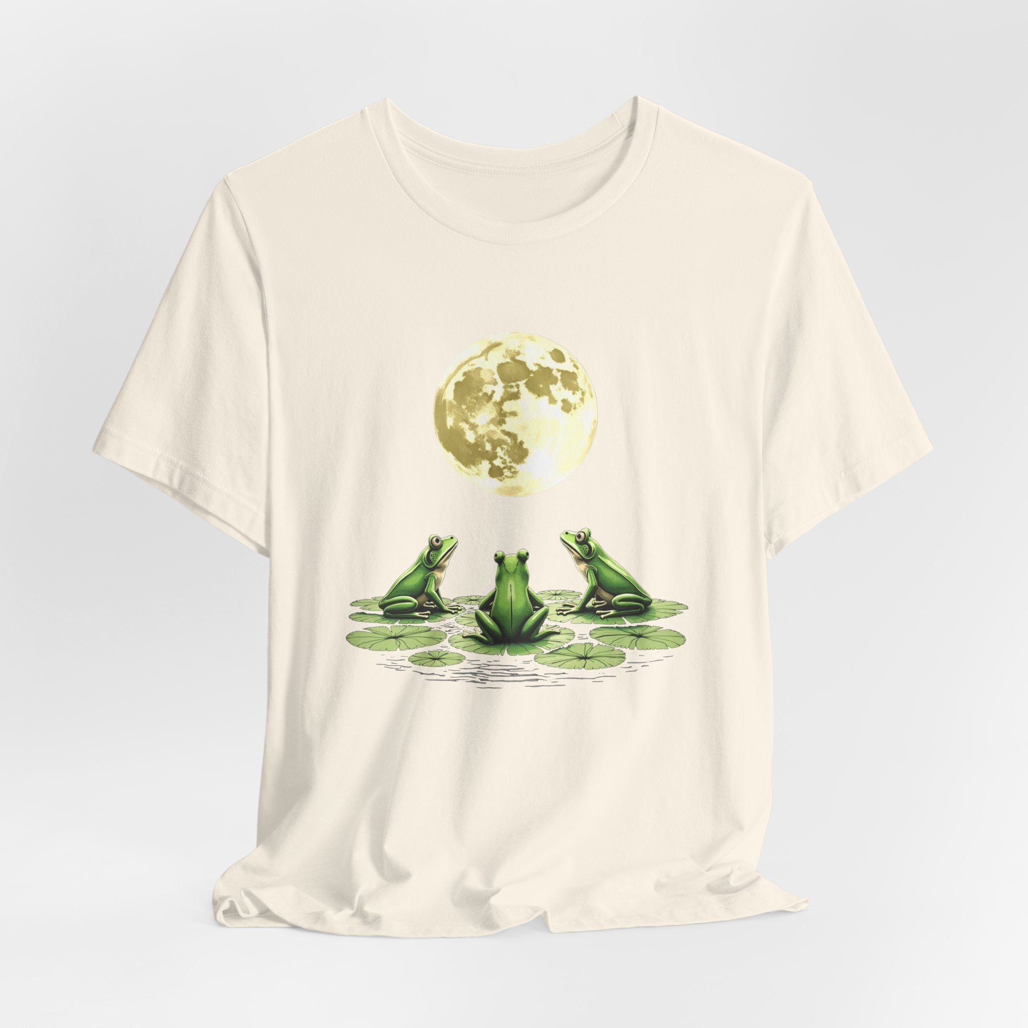 Ivory beige t-shirt featuring cute frogs sitting on top of water lily watching on the moon graphic on a white background