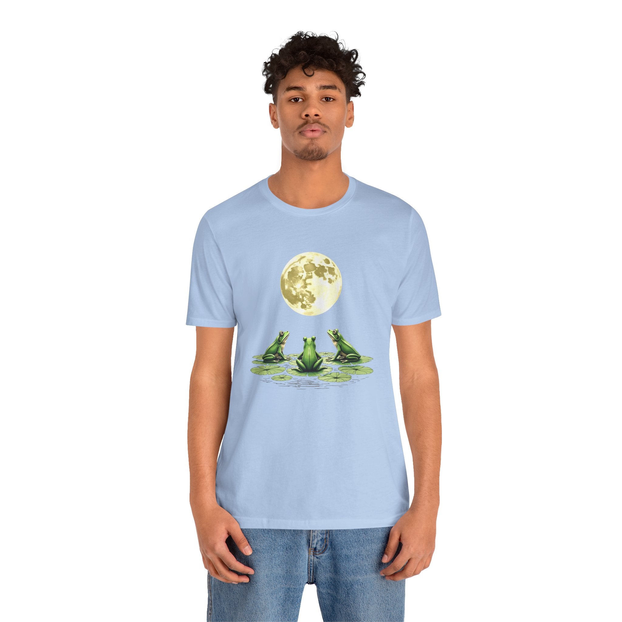 Person wearing a light blue t-shirt with a graphic of three frogs and a moon.