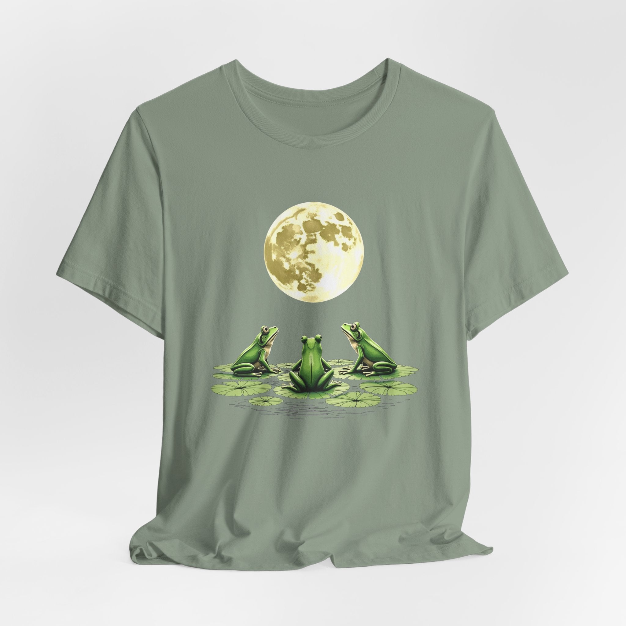 Sage green t-shirt featuring cute frogs sitting on top of water lily watching on the moon graphic on a white background