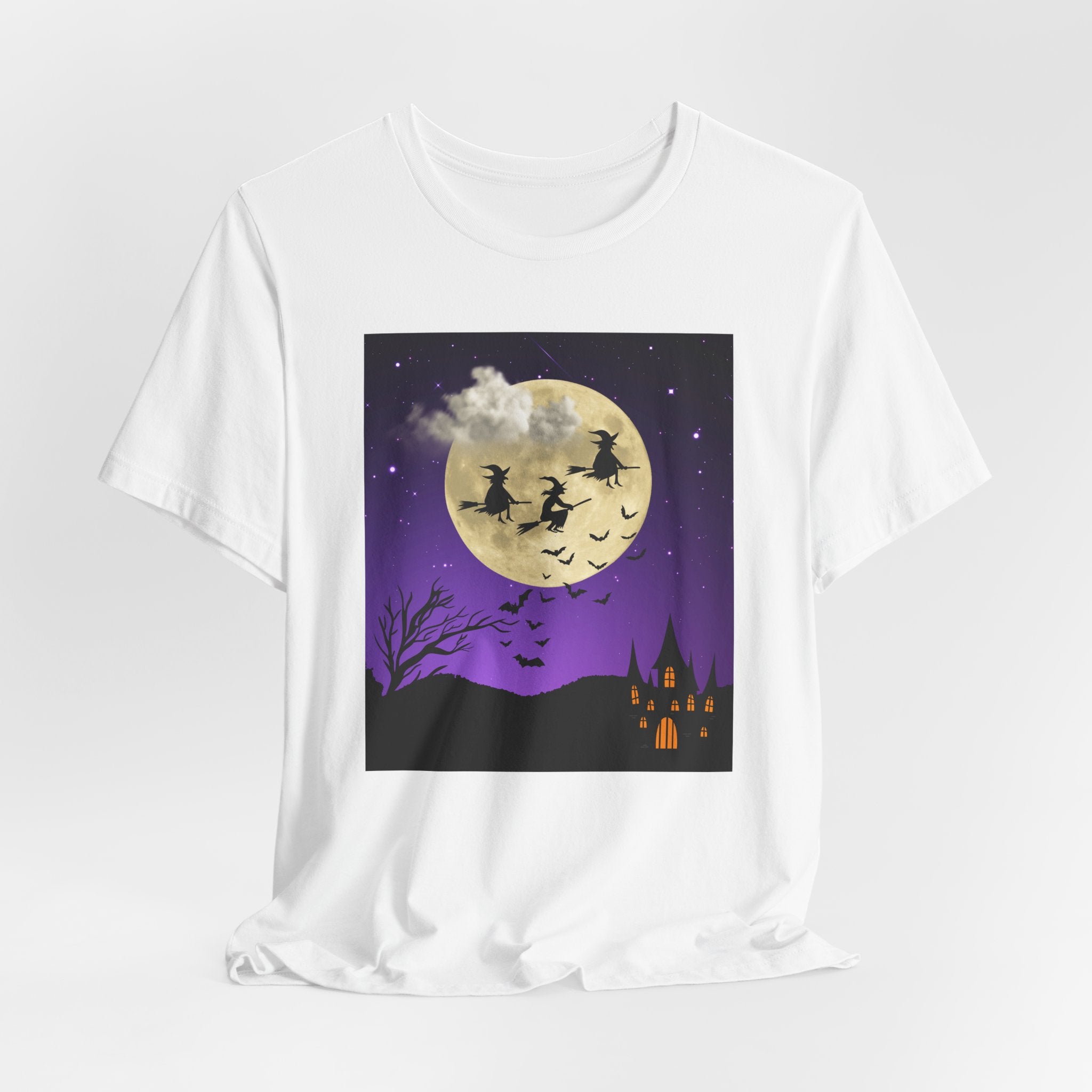 White t-shirt with Halloween-themed graphic of witches flying over a moonlit sky with a castle.