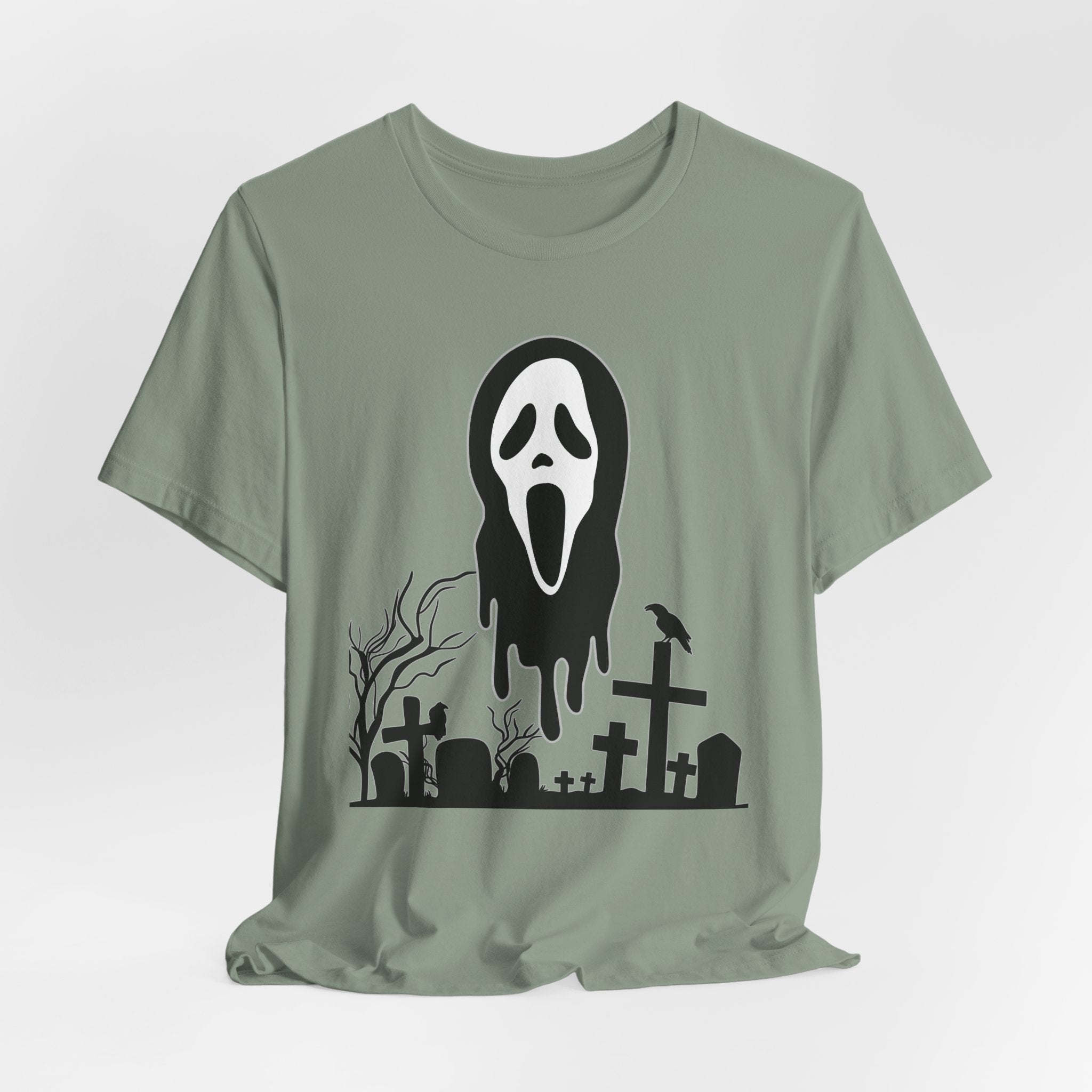 Sage green t-shirt with a black graphic design of a ghost face and graveyard on a white background