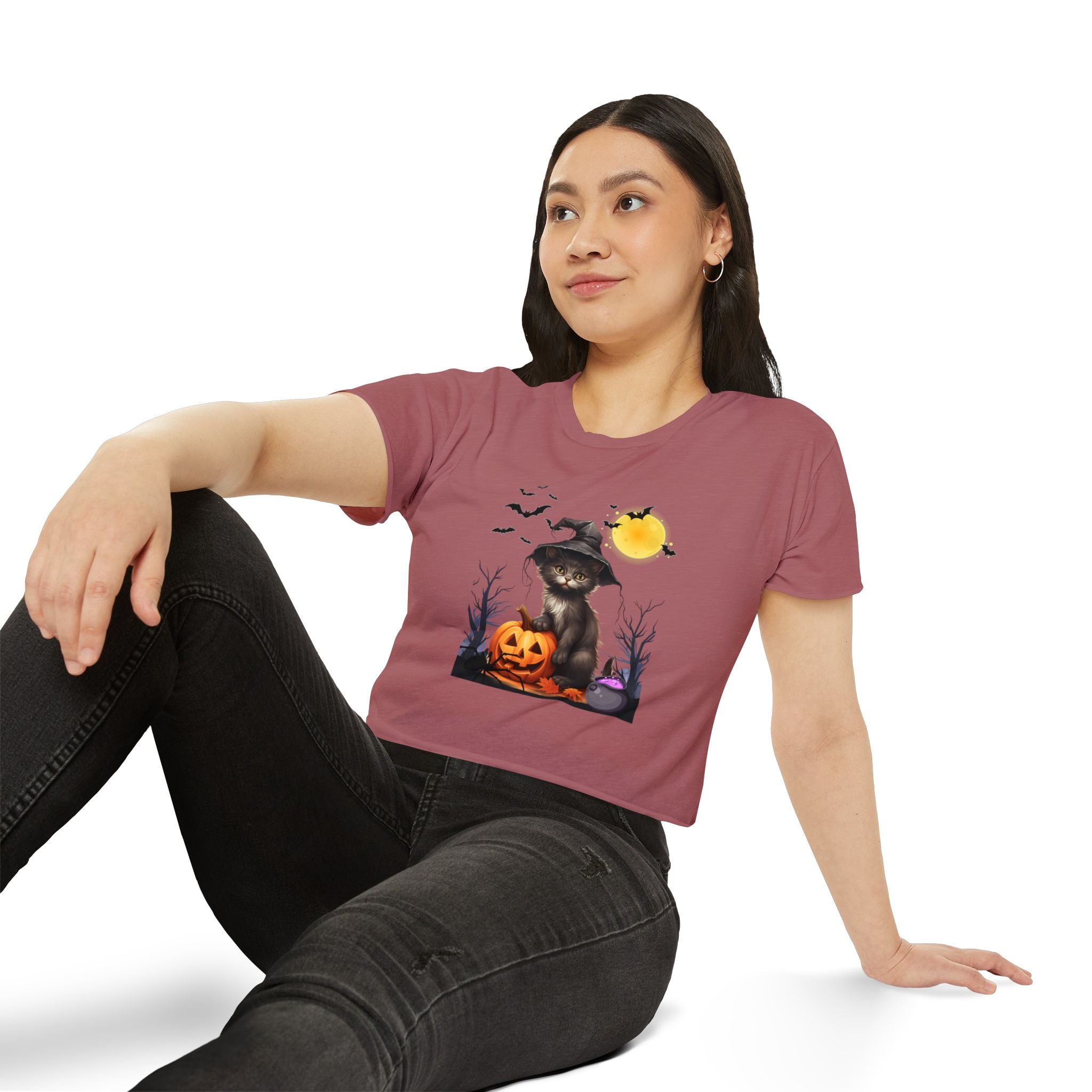 Woman wearing a pink t-shirt with a Halloween-themed design featuring a cat, pumpkins, and bats.