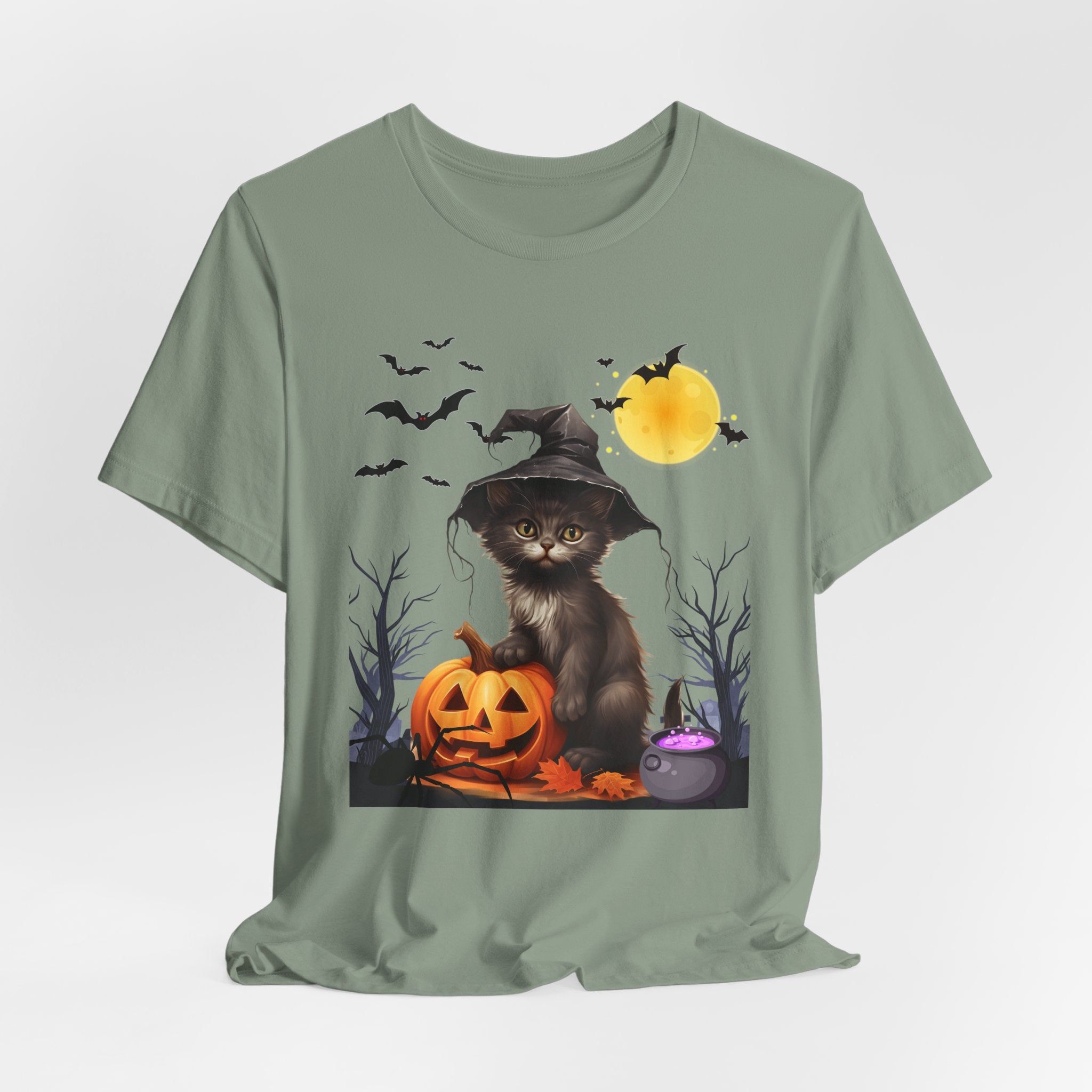 Sage green t-shirt with a Halloween-themed design featuring a cat in a witch hat, pumpkins, and bats on a white background.