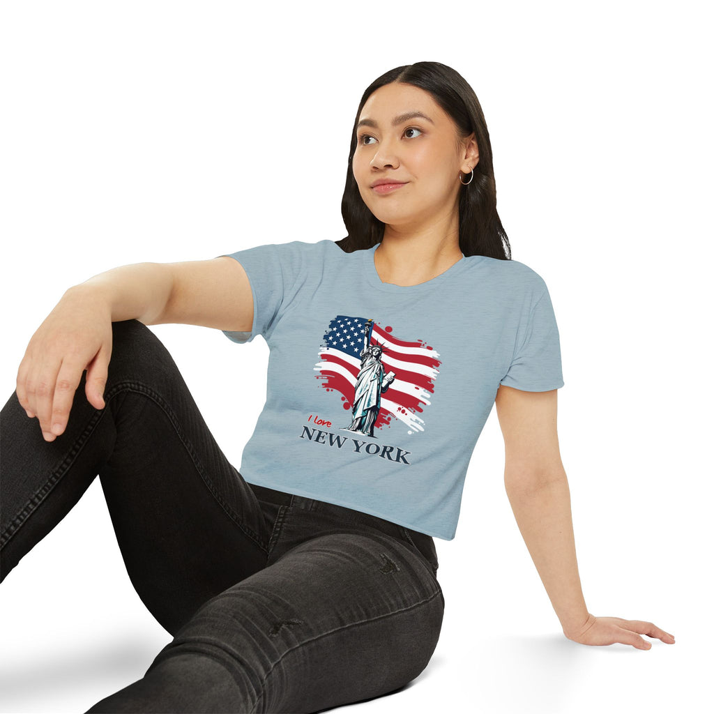 Woman wearing a light blue t-shirt with a graphic design of the Statue of Liberty and American flag, sitting on a white background.