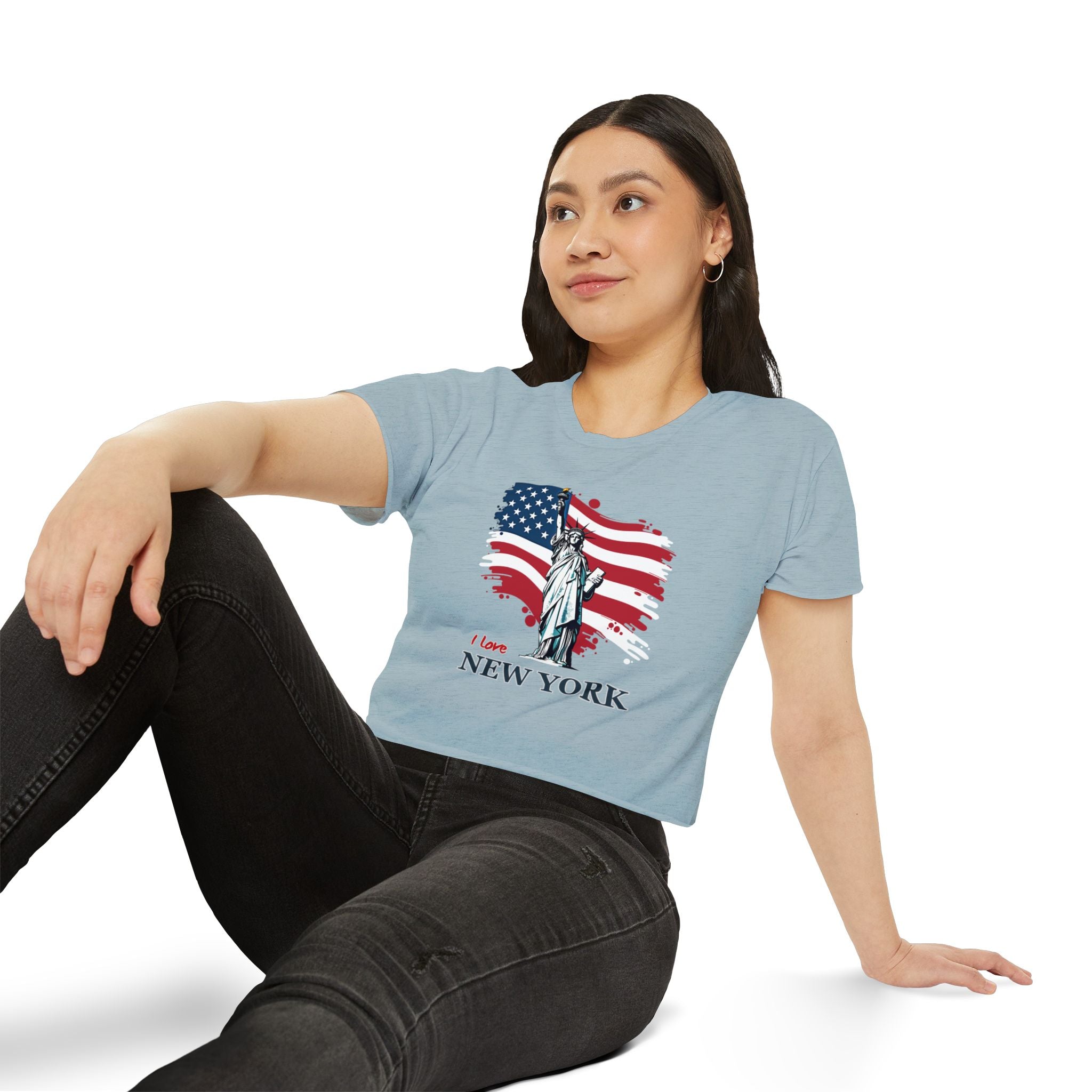 Woman wearing a light blue t-shirt with a graphic design of the Statue of Liberty and American flag, sitting on a white background.