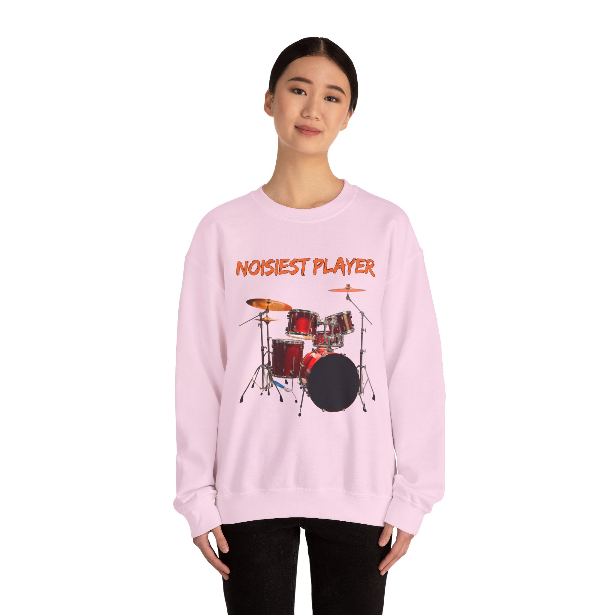 A female standing wearing light pink sweatshirt with drum set graphic and 'NOISIEST PLAYER' text on a white background