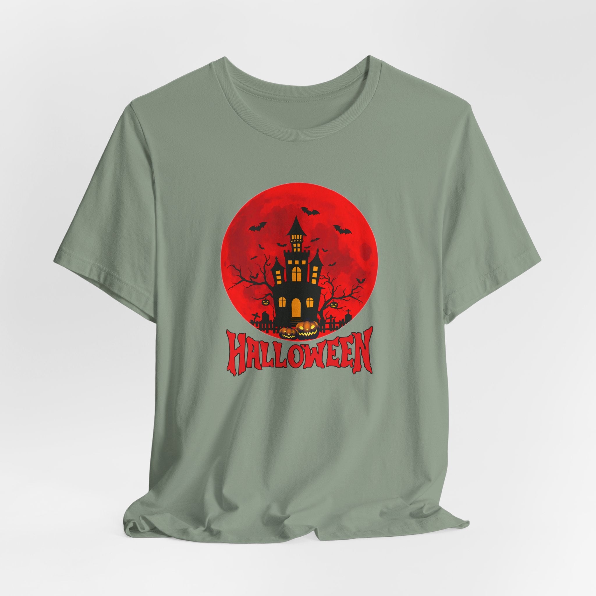Sage green t-shirt with Halloween graphic featuring a castle, pumpkin, bats under the red moon and 'Halloween' text on a white background