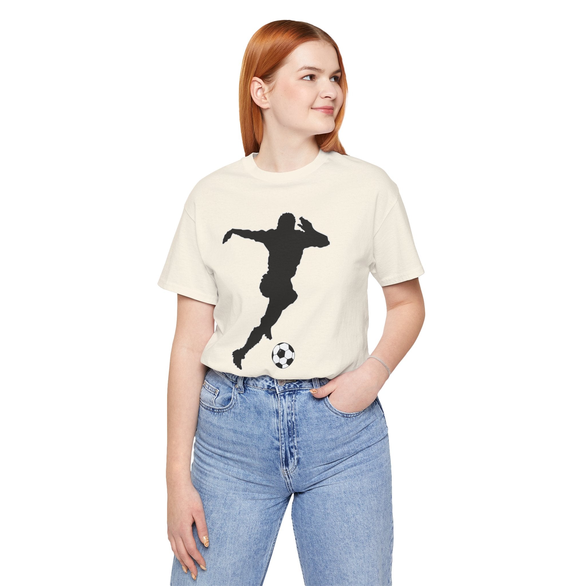 Person wearing a cream t-shirt with a black silhouette design of a person playing soccer, standing against a white background.