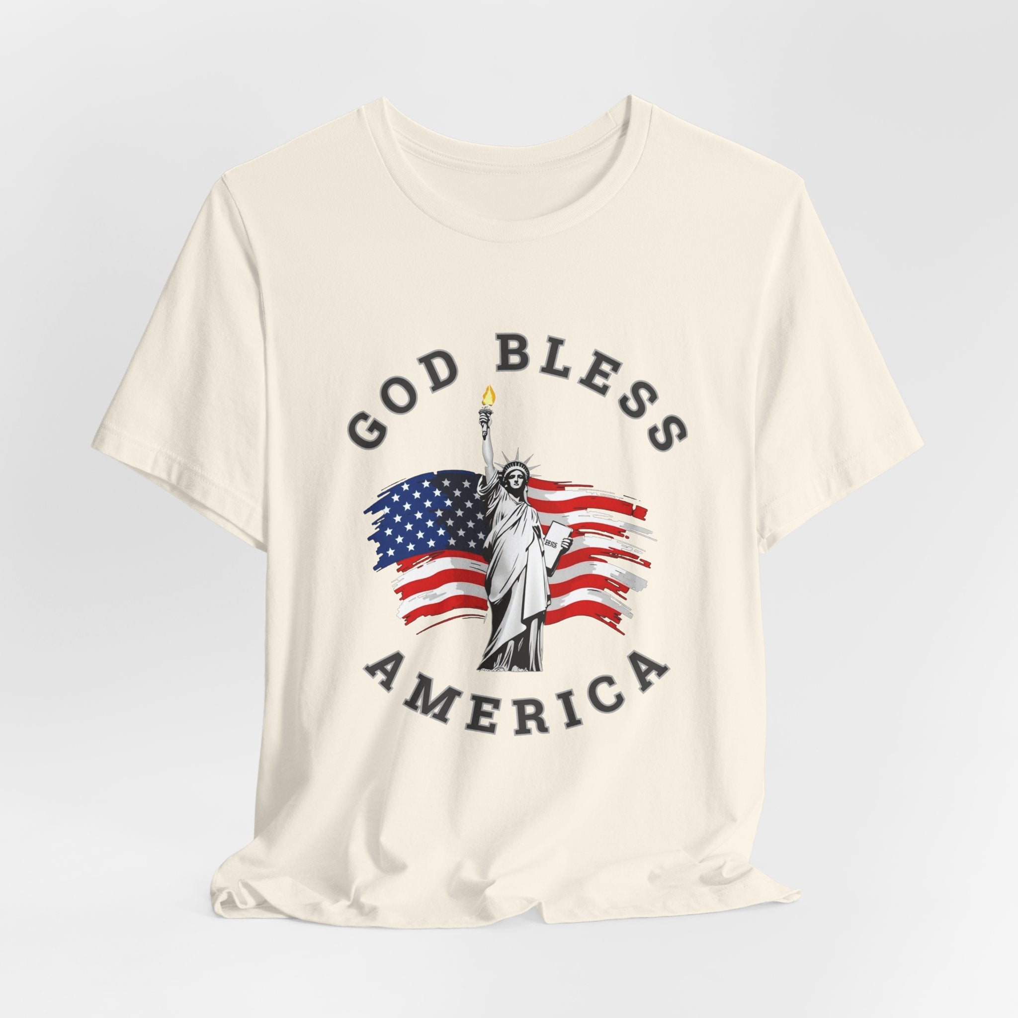 Natural beige t-shirt with 'God Bless America' graphic featuring the Statue of Liberty and American flag on a light gray background.