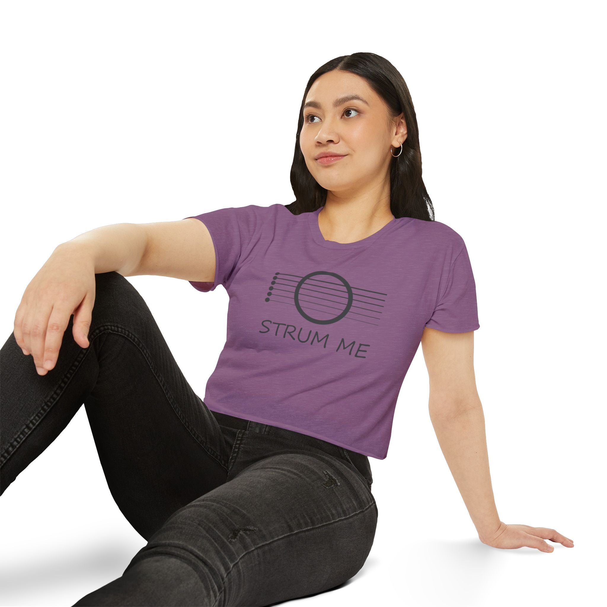 Woman wearing a purple t-shirt with 'STRUM ME' text and graphic, sitting on a white background